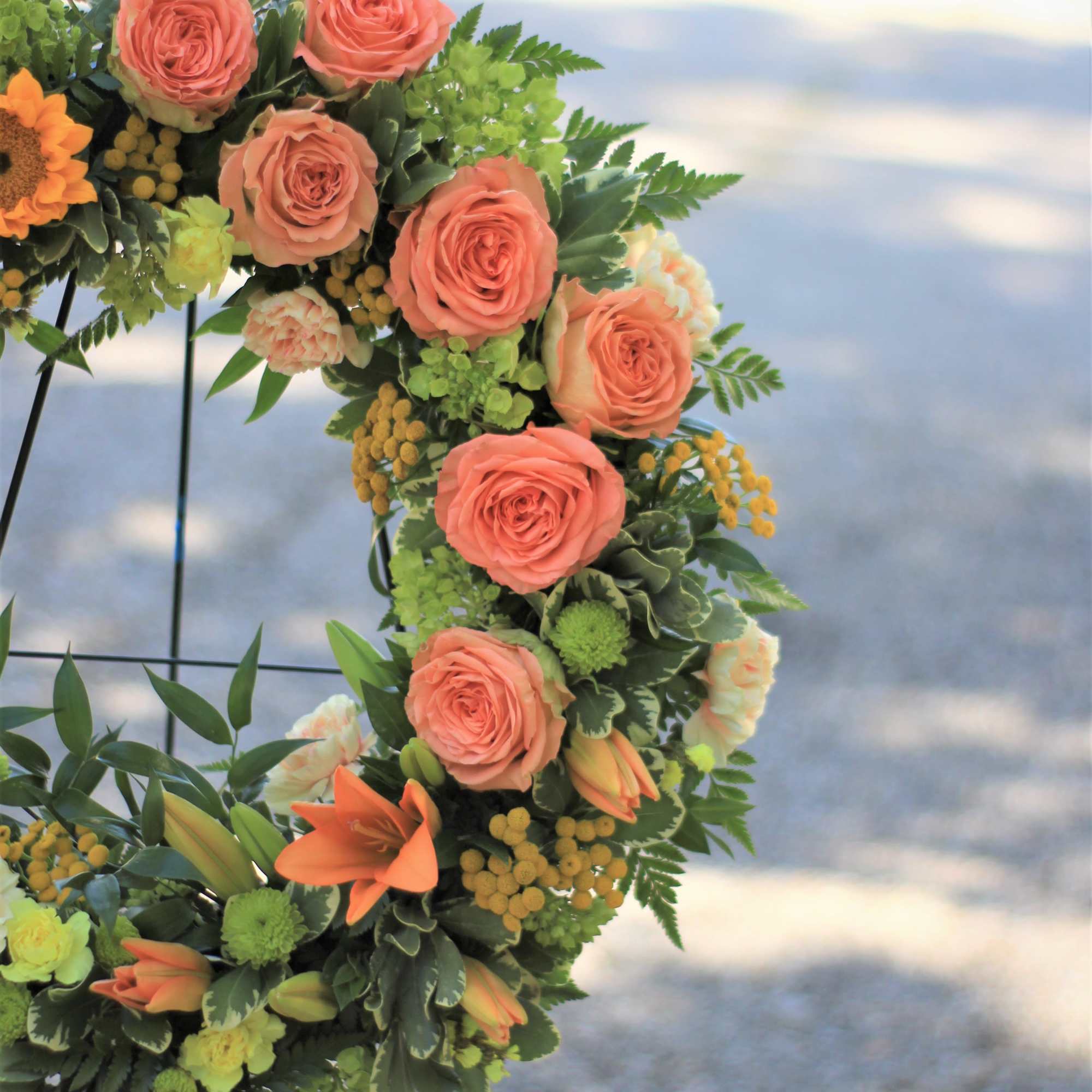 Floral wreath with peach roses and orange blooms on a metal stand