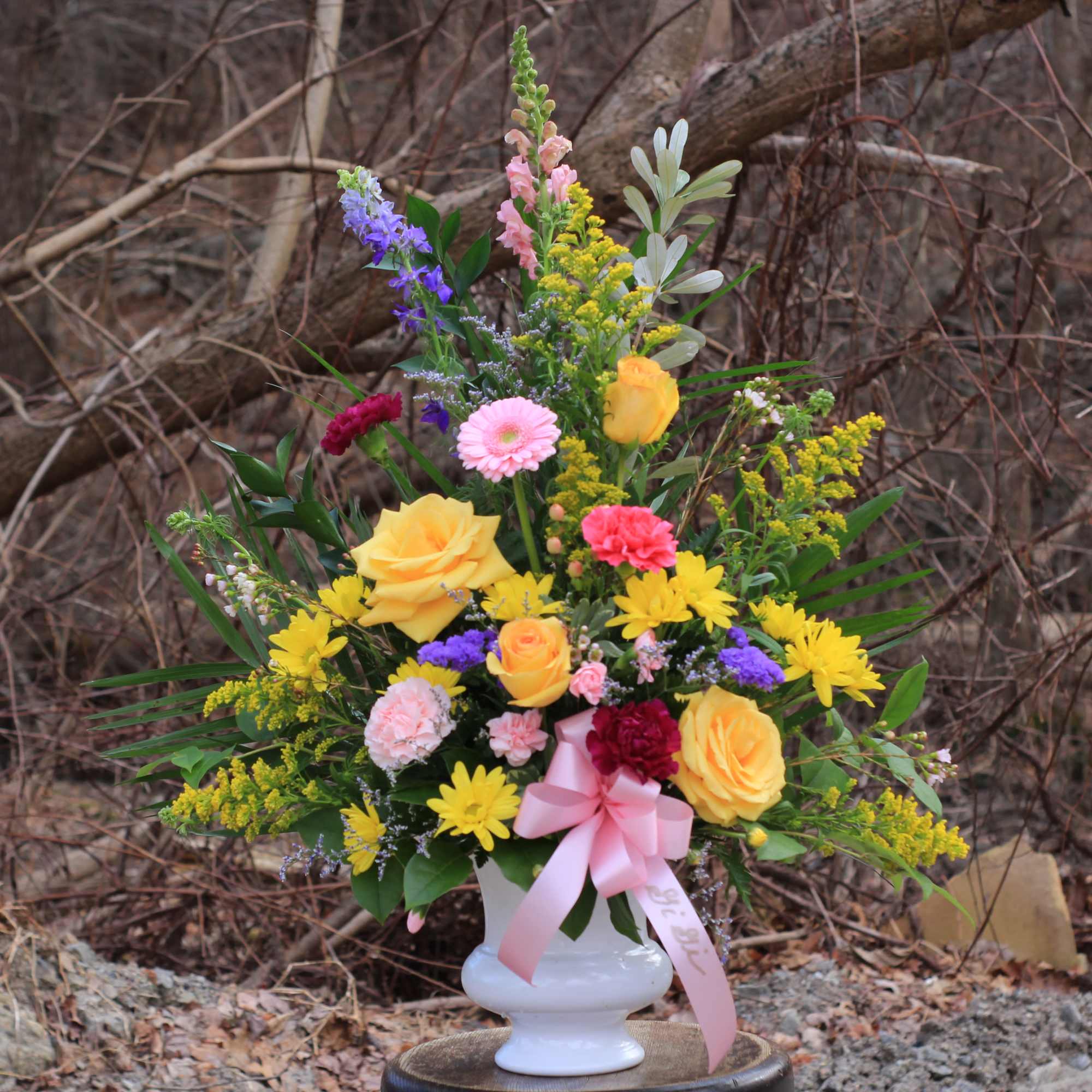 Colorful mixed flower arrangement in a white vase with a pink ribbon
