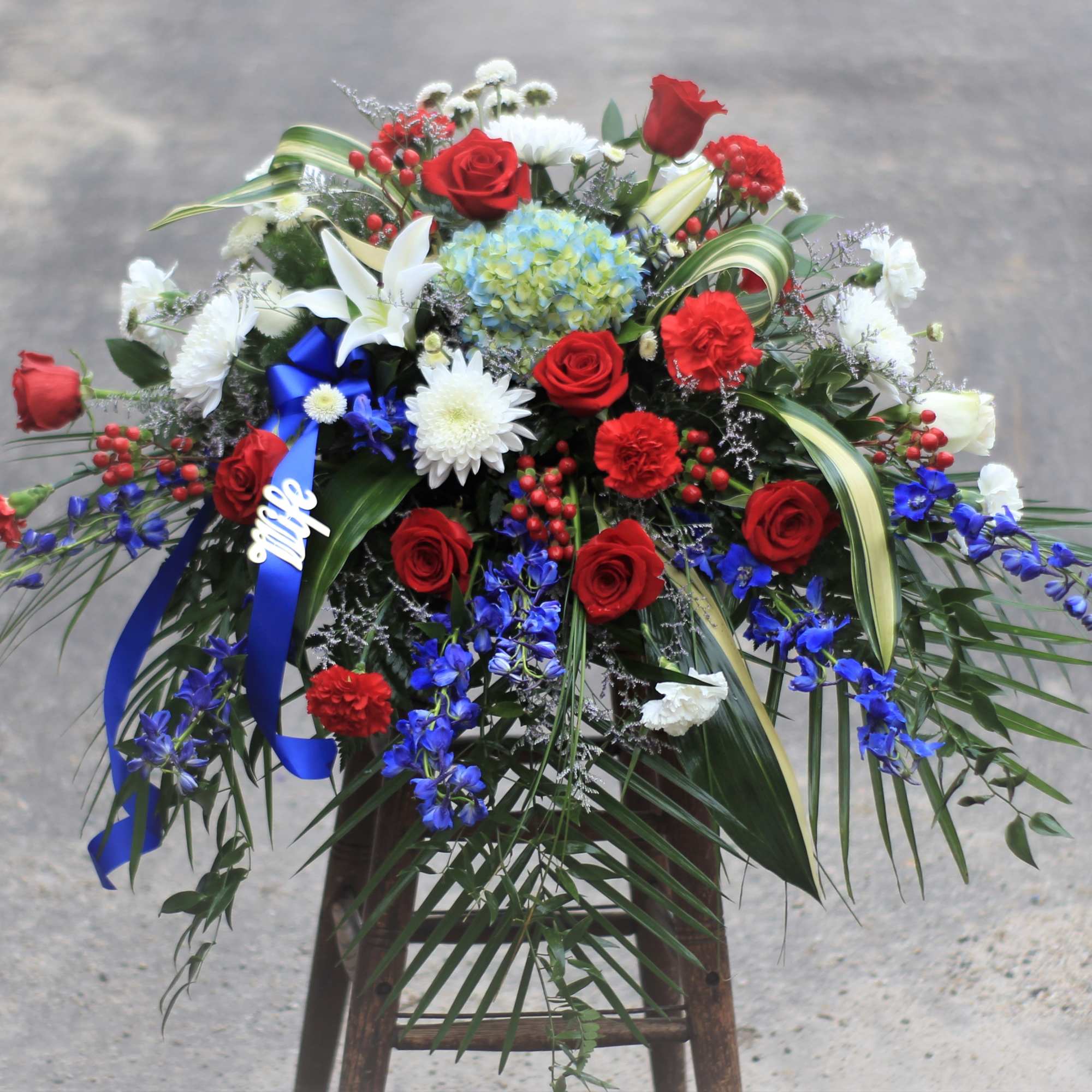 Large floral arrangement with red roses, white lilies, and blue flowers on a stand