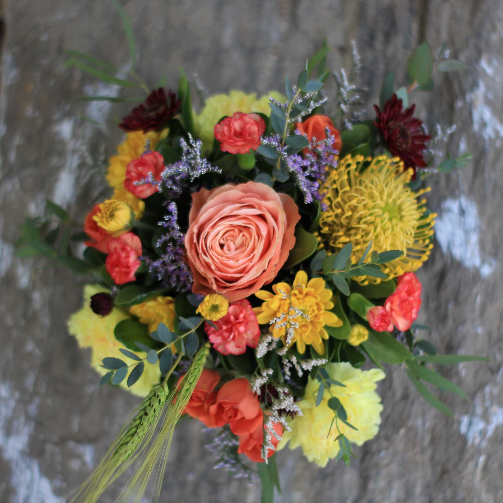 Round bouquet with a peach rose and mixed yellow, coral, and burgundy flowers