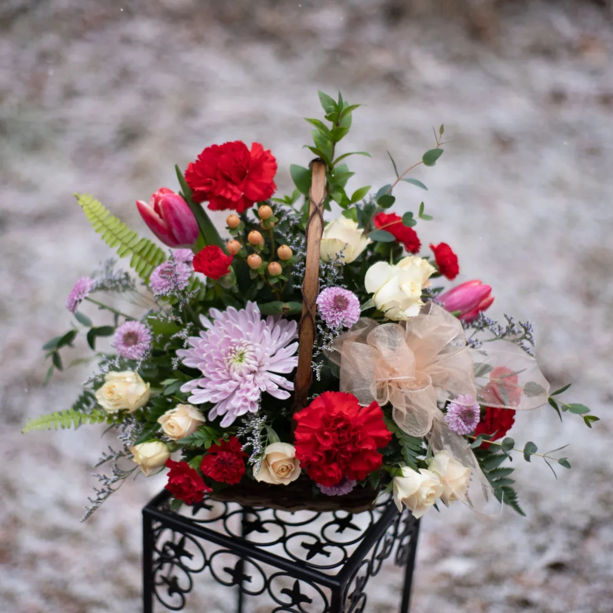 Basket arrangement of red, cream, and lavender flowers with a ribbon bow