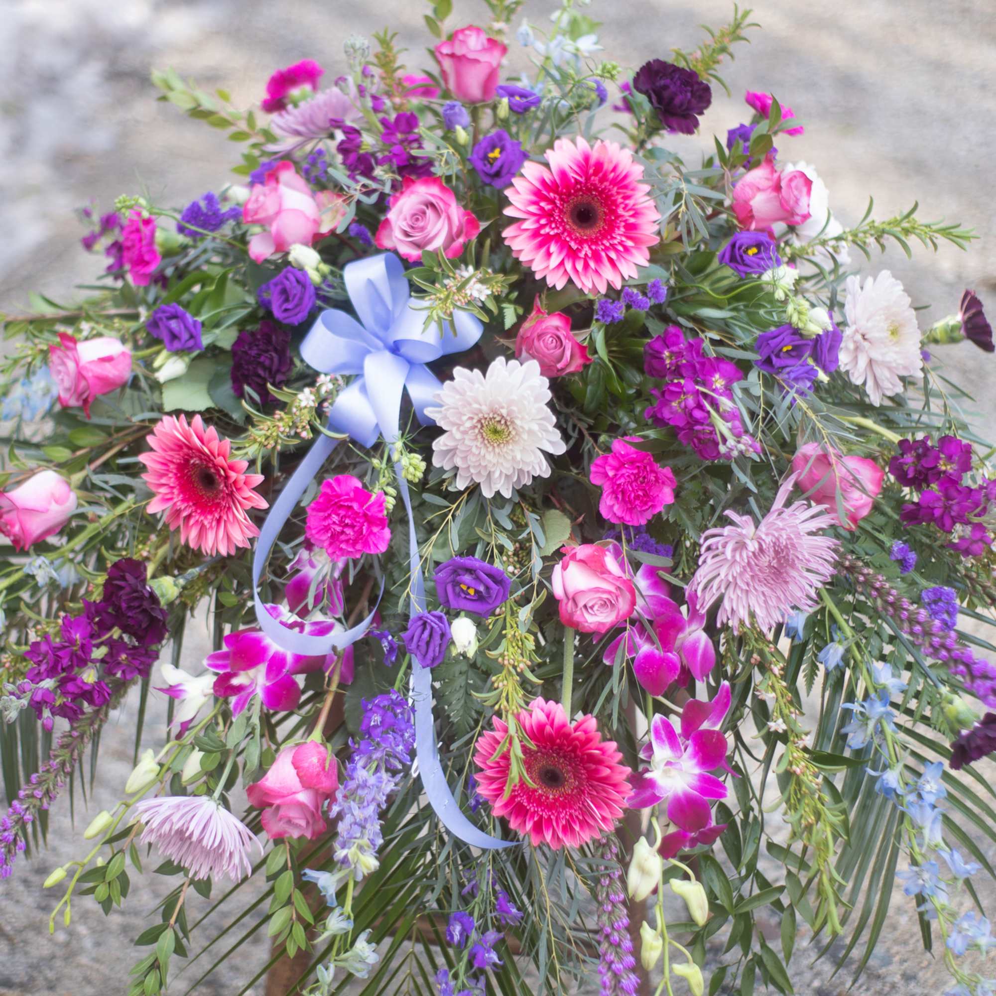 Large bouquet of pink, purple, and white flowers with a blue ribbon