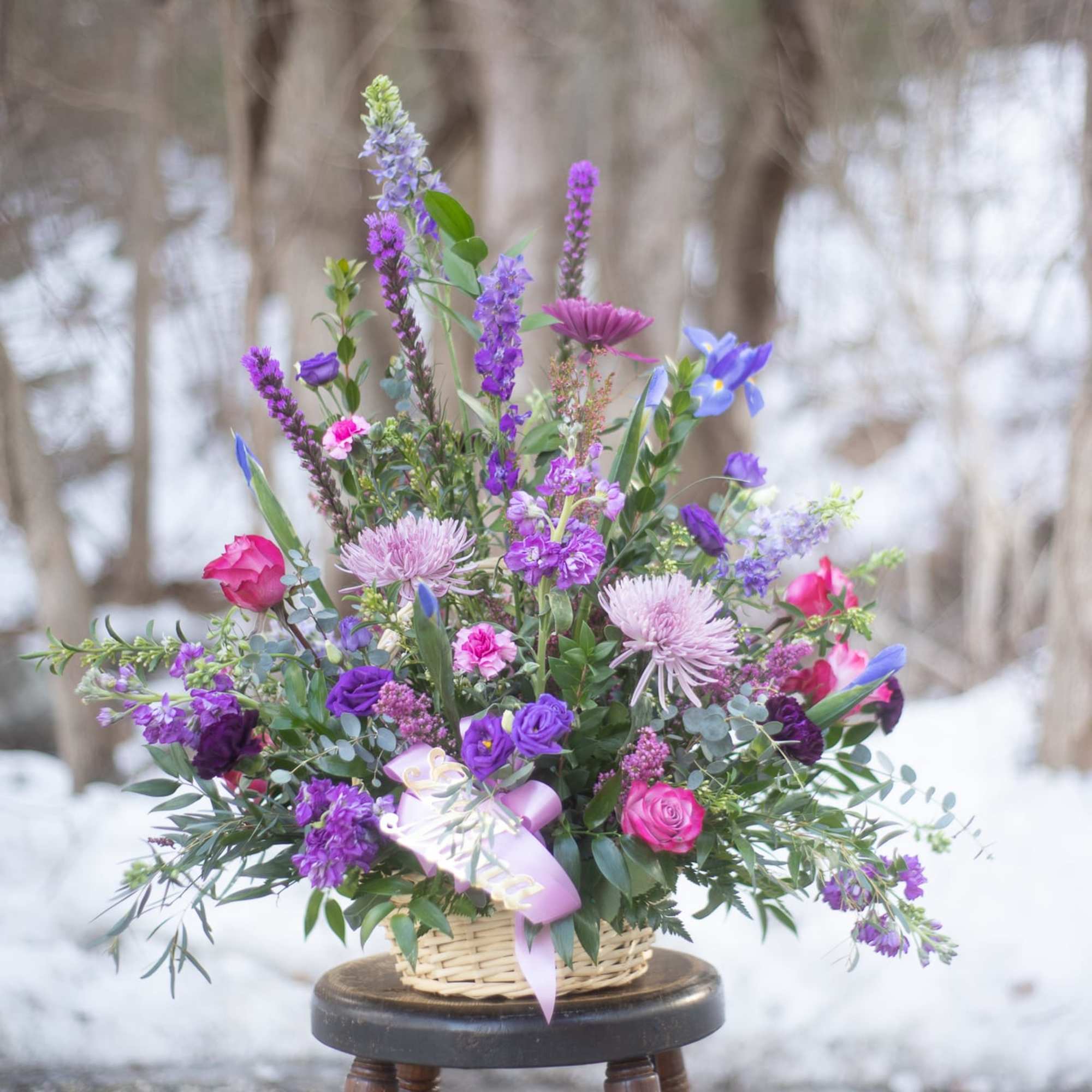 Mixed purple and pink flower arrangement in a wicker basket