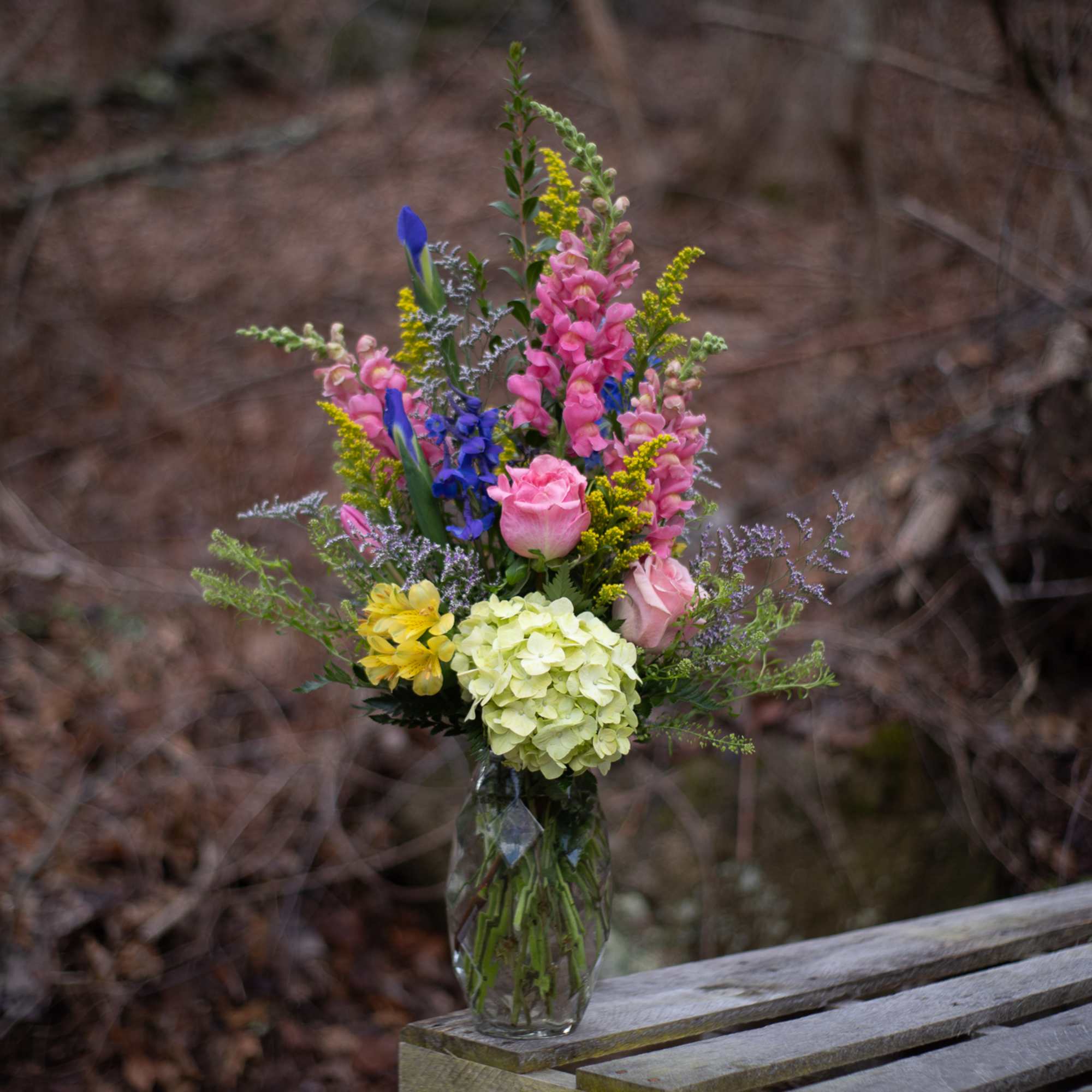 Mixed bouquet in a clear glass vase with pink, blue, yellow, and white flowers