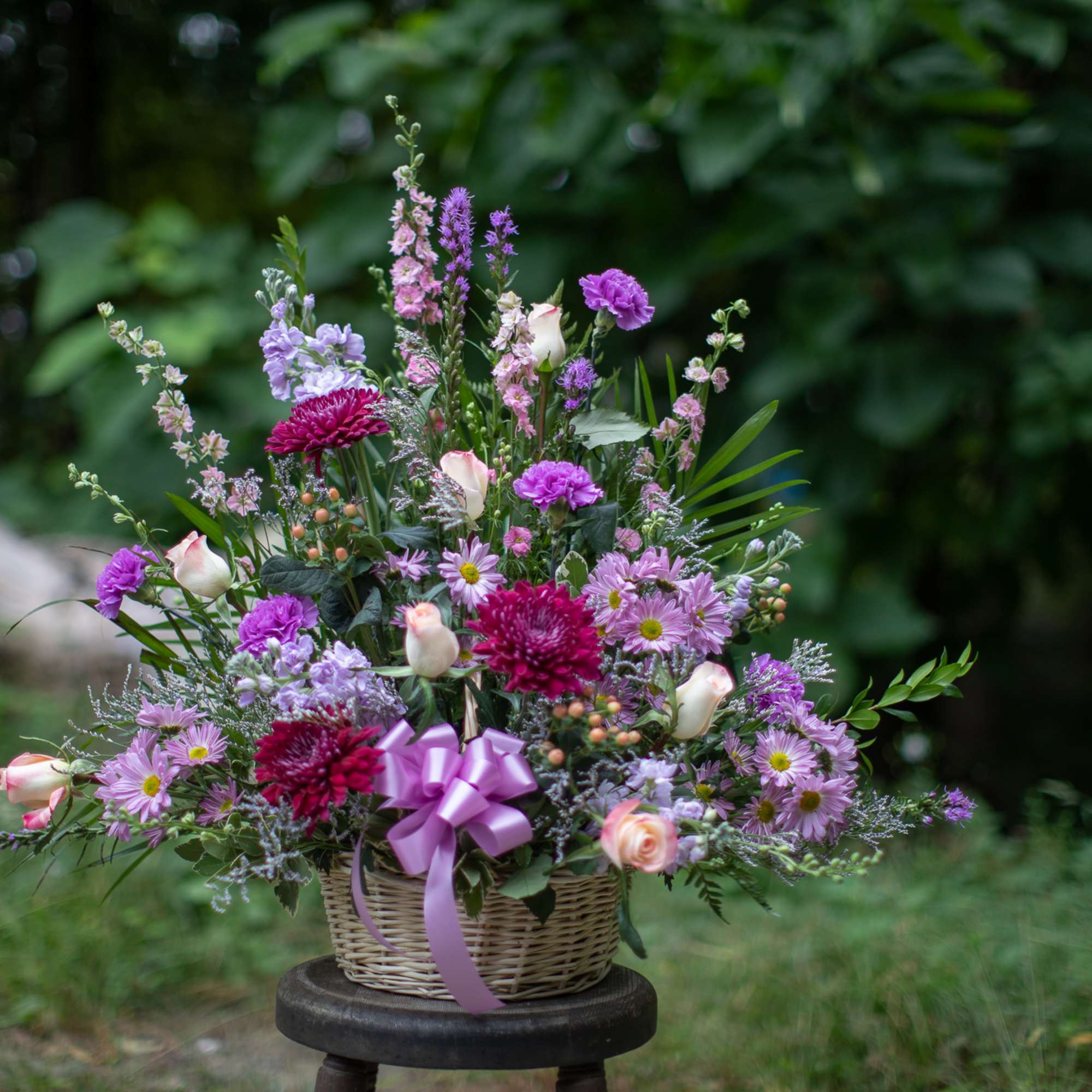 Basket arrangement of pink and purple flowers with a ribbon bow