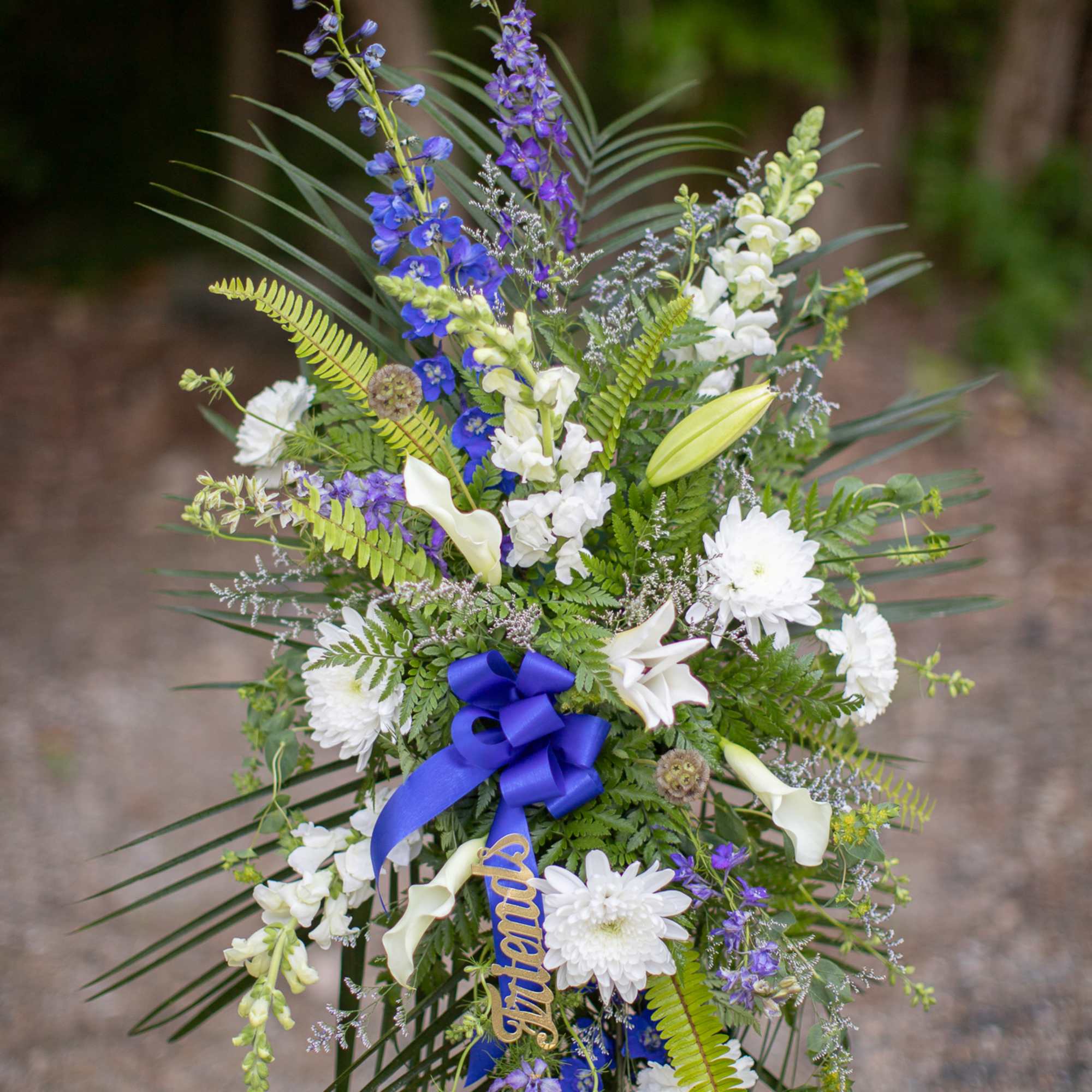 Tall floral standing spray with white and blue flowers and a blue ribbon