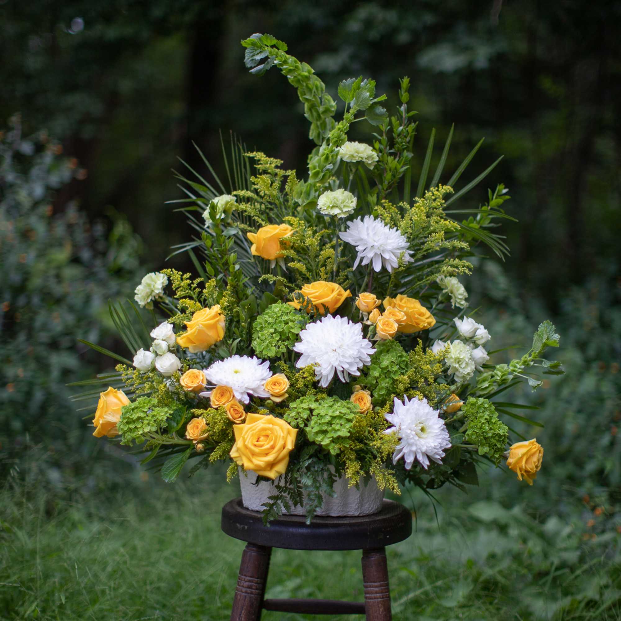 Yellow roses and white mums arranged in a white container on a stool