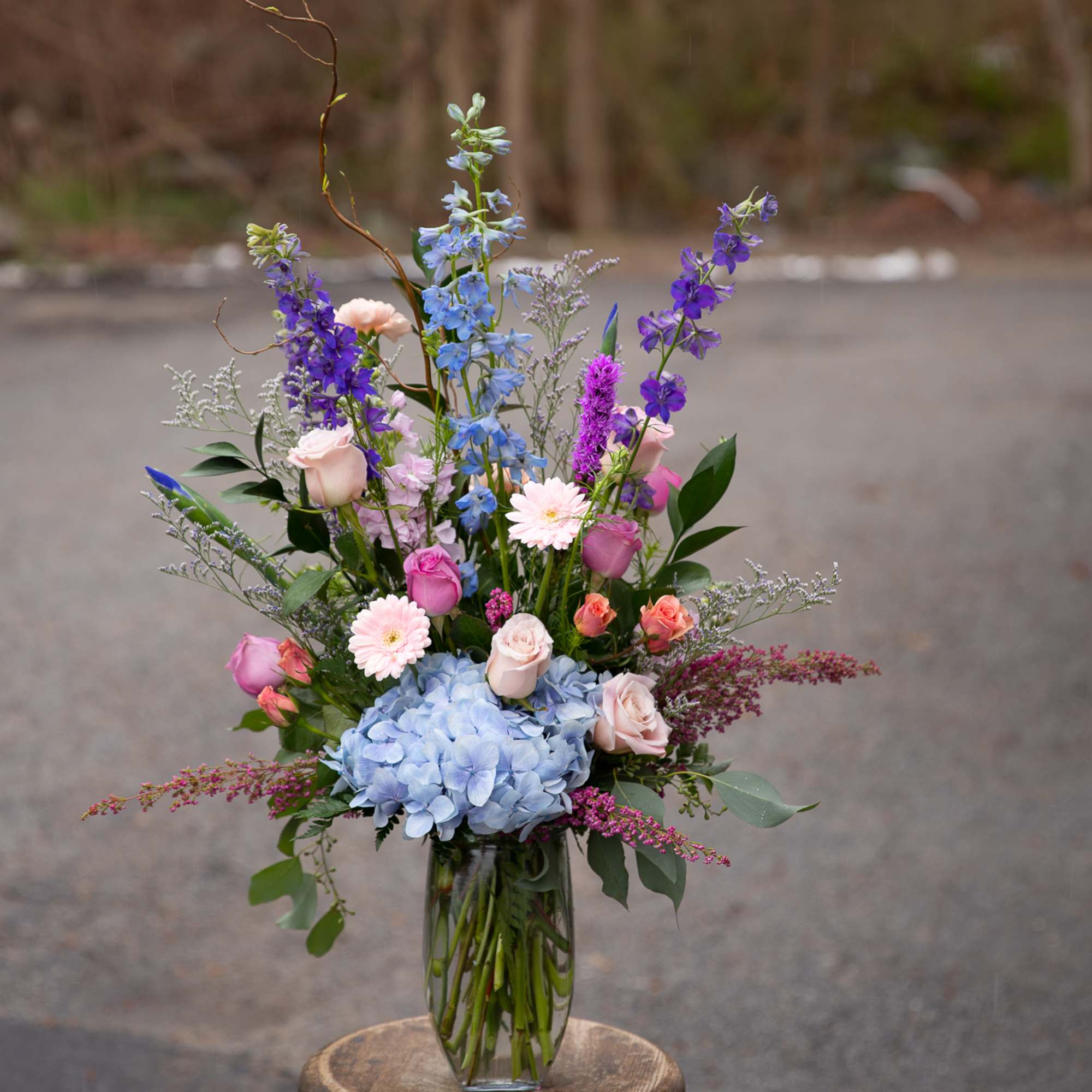 Tall mixed bouquet in a clear glass vase with blue hydrangea and purple flowers