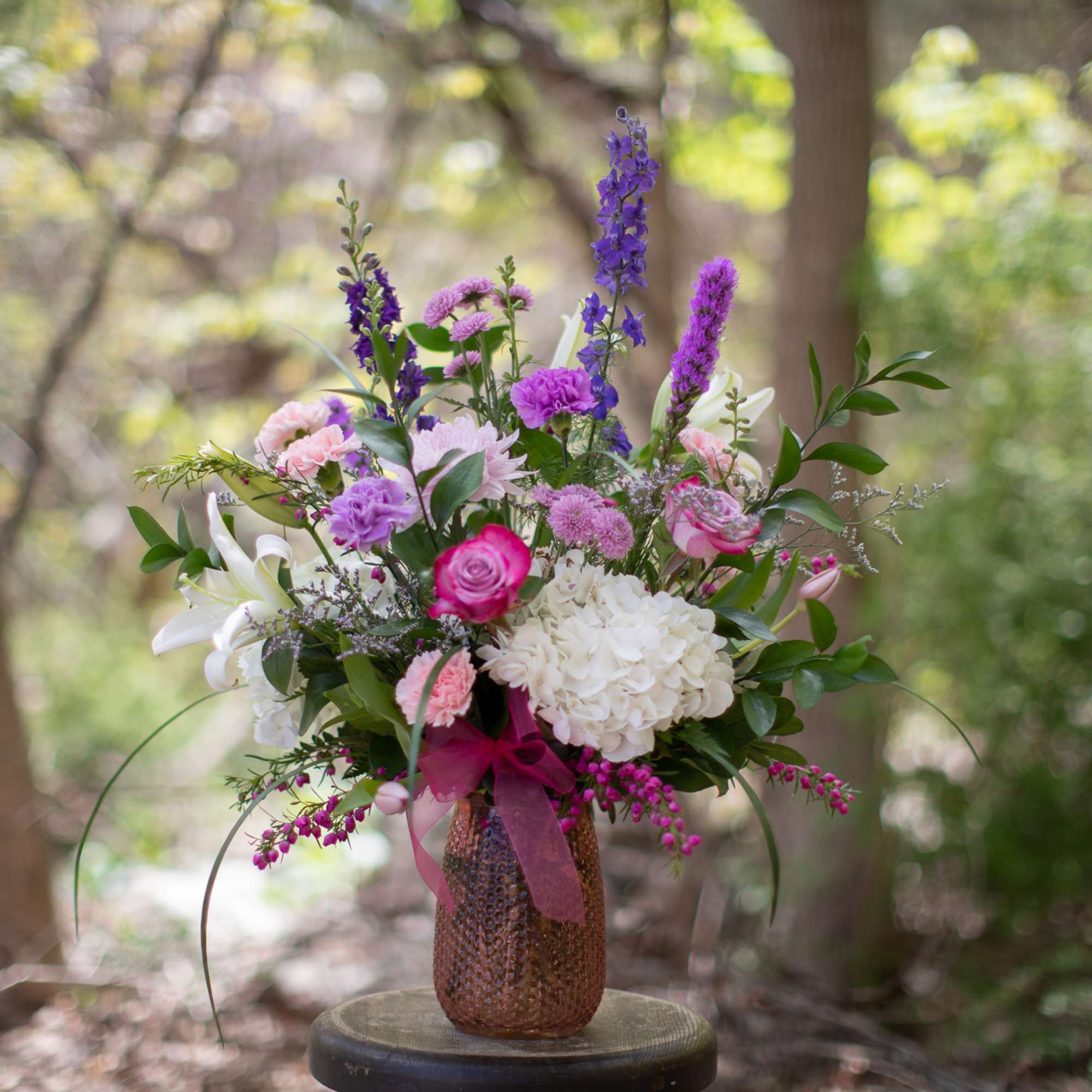 Mixed bouquet of pink, purple, and white flowers in a textured vase