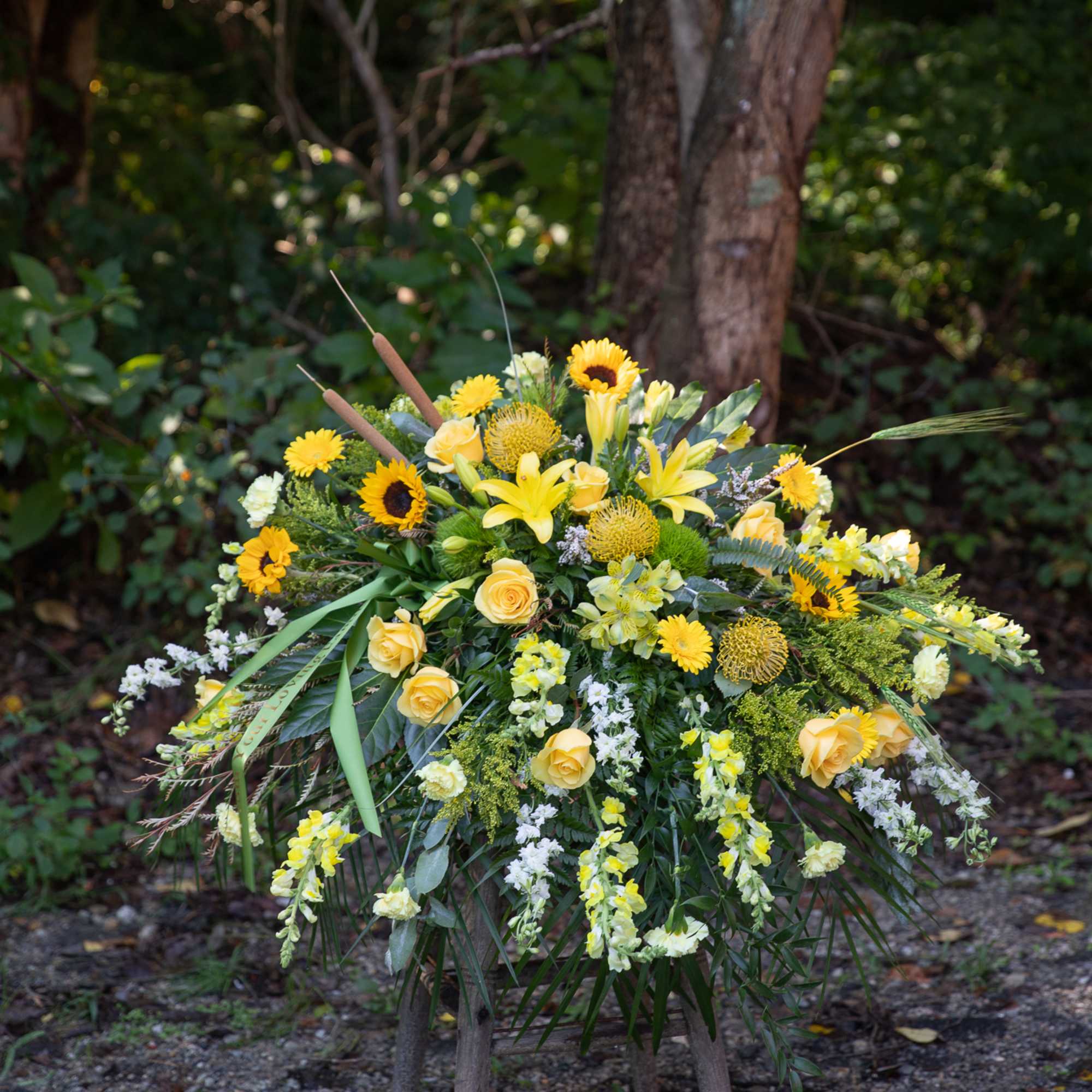 Yellow floral spray with roses, lilies, and sunflowers on a stand