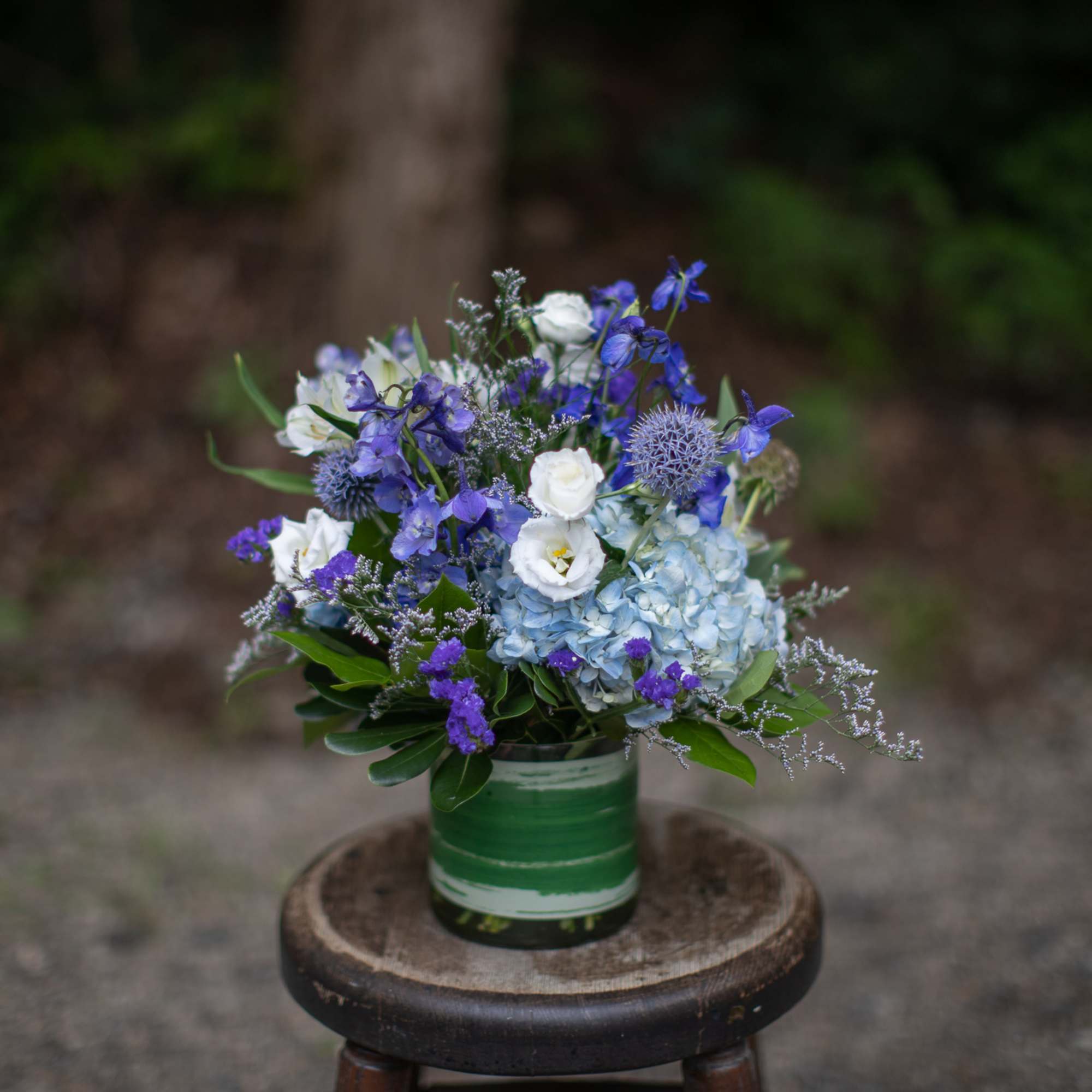 Blue and white floral arrangement in a green-striped container