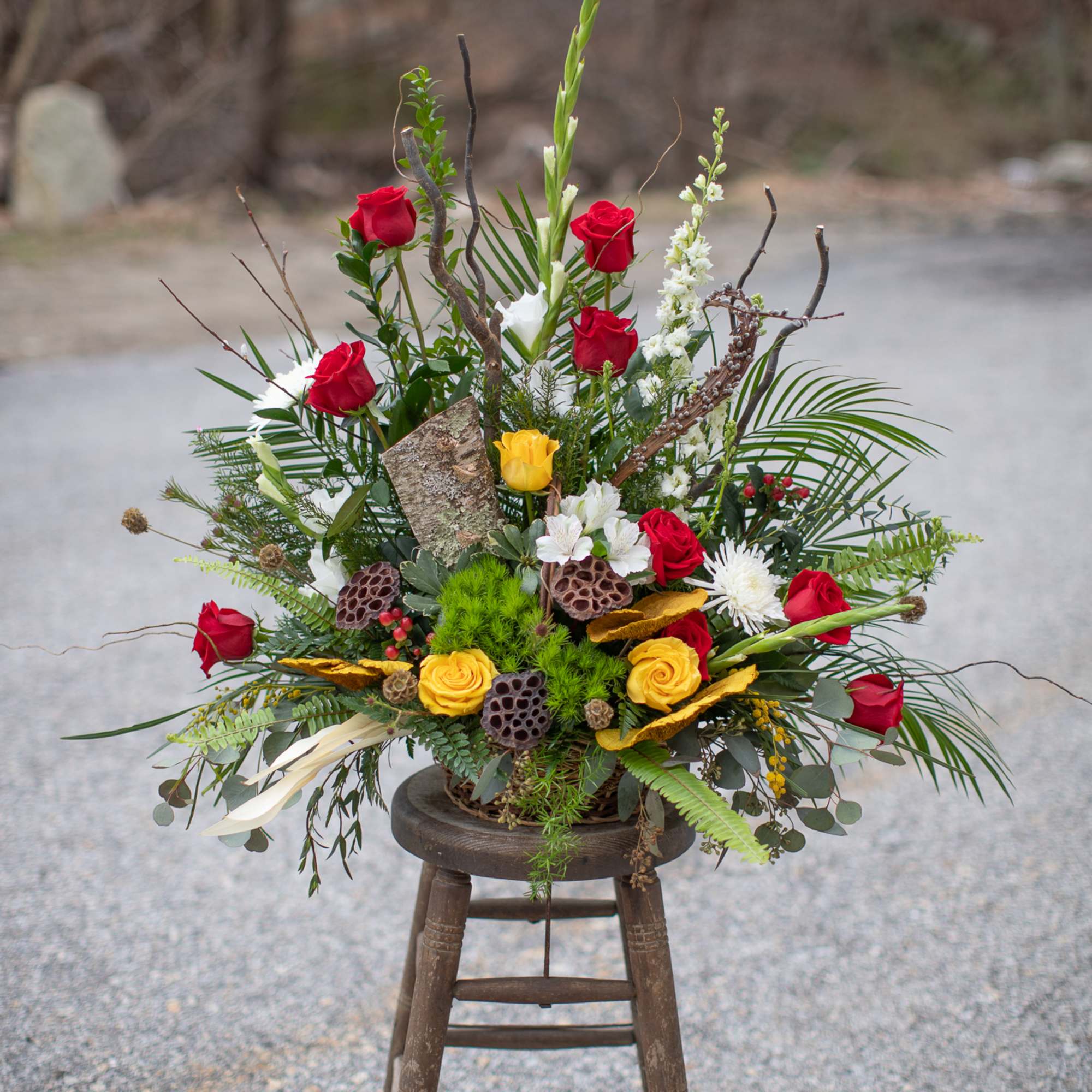 Tall floral arrangement with red and yellow roses in a rustic container