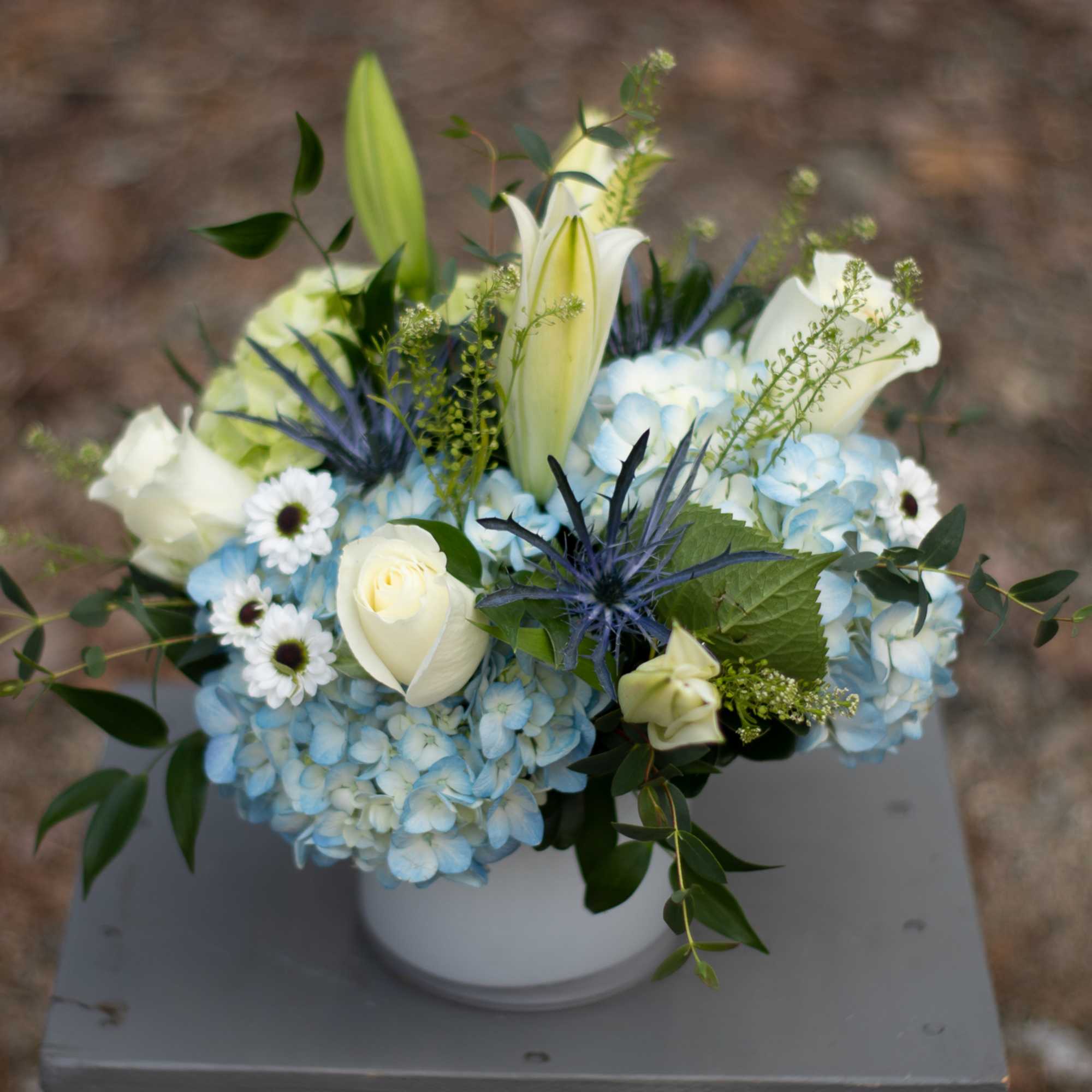 Blue hydrangea arrangement with white lilies and roses in a white vase