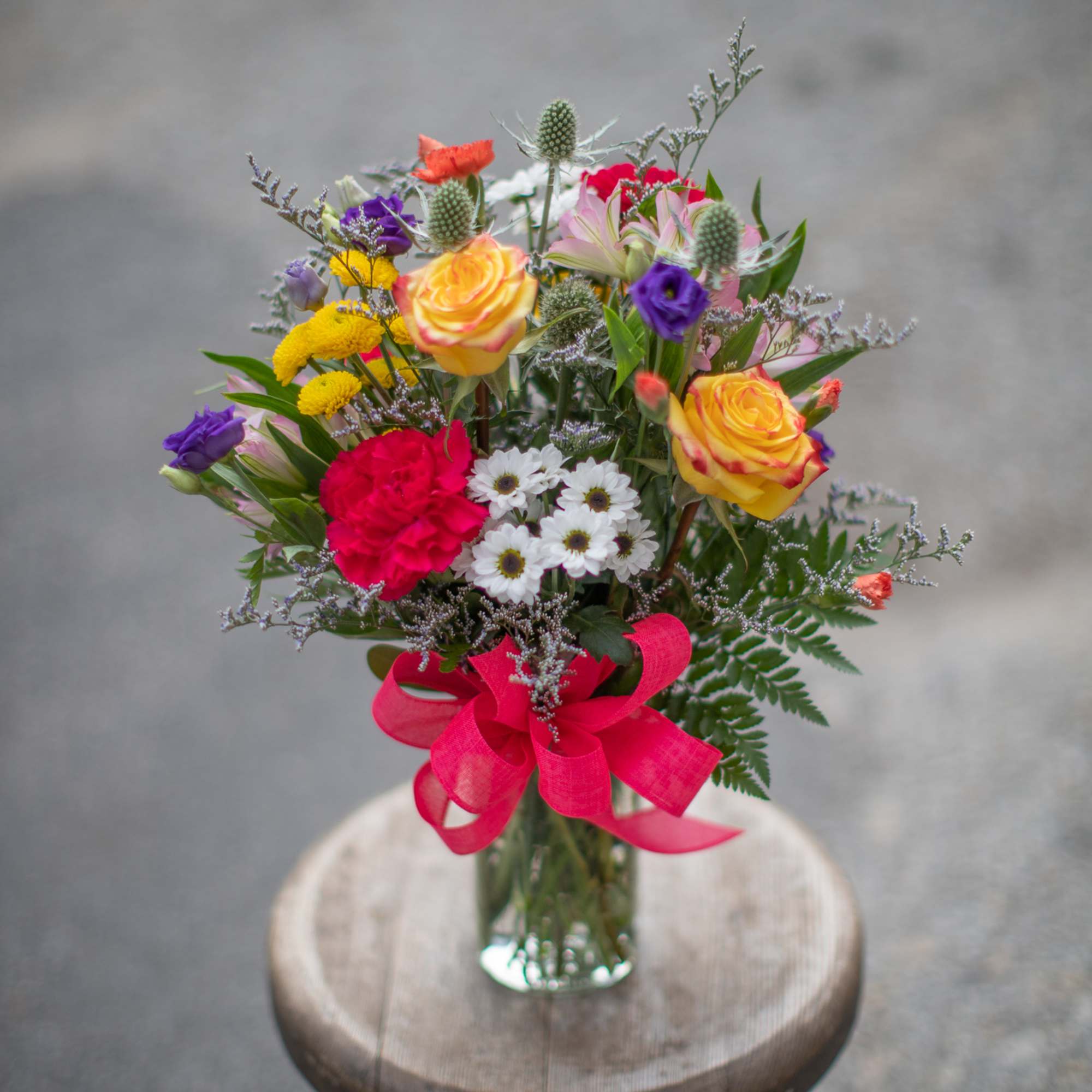 Mixed bouquet of colorful flowers in a clear glass vase with a pink ribbon