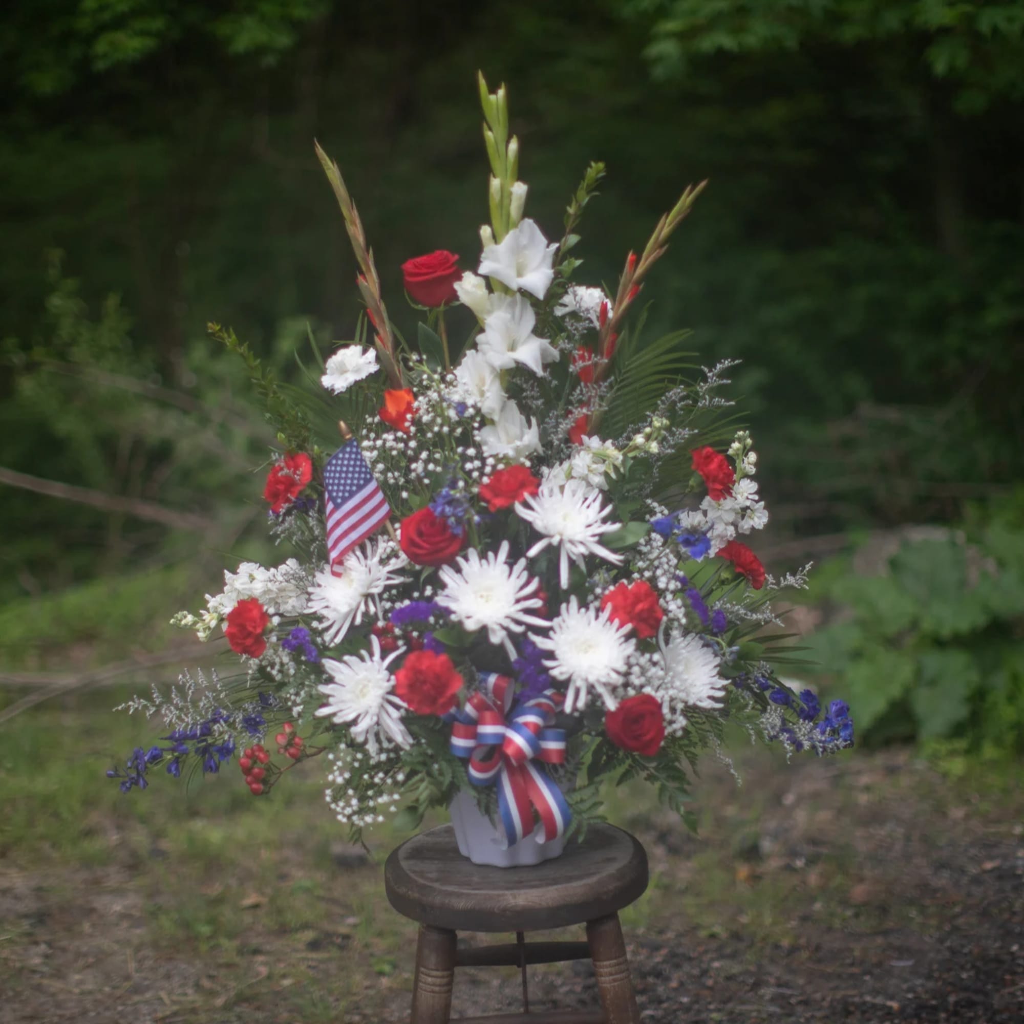 Red, white, and blue floral arrangement in a white vase with a ribbon