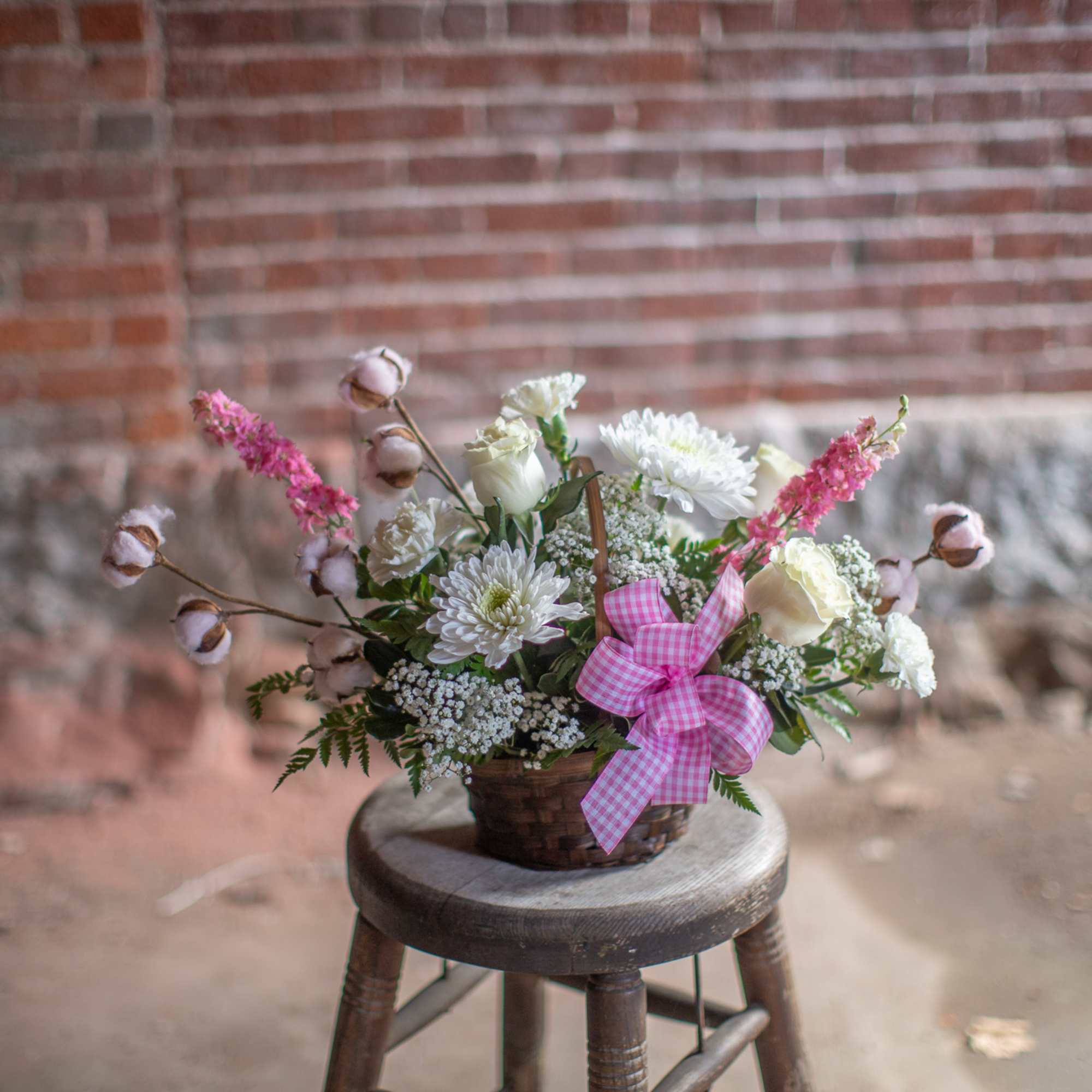 Basket arrangement of white and pink flowers with a gingham ribbon