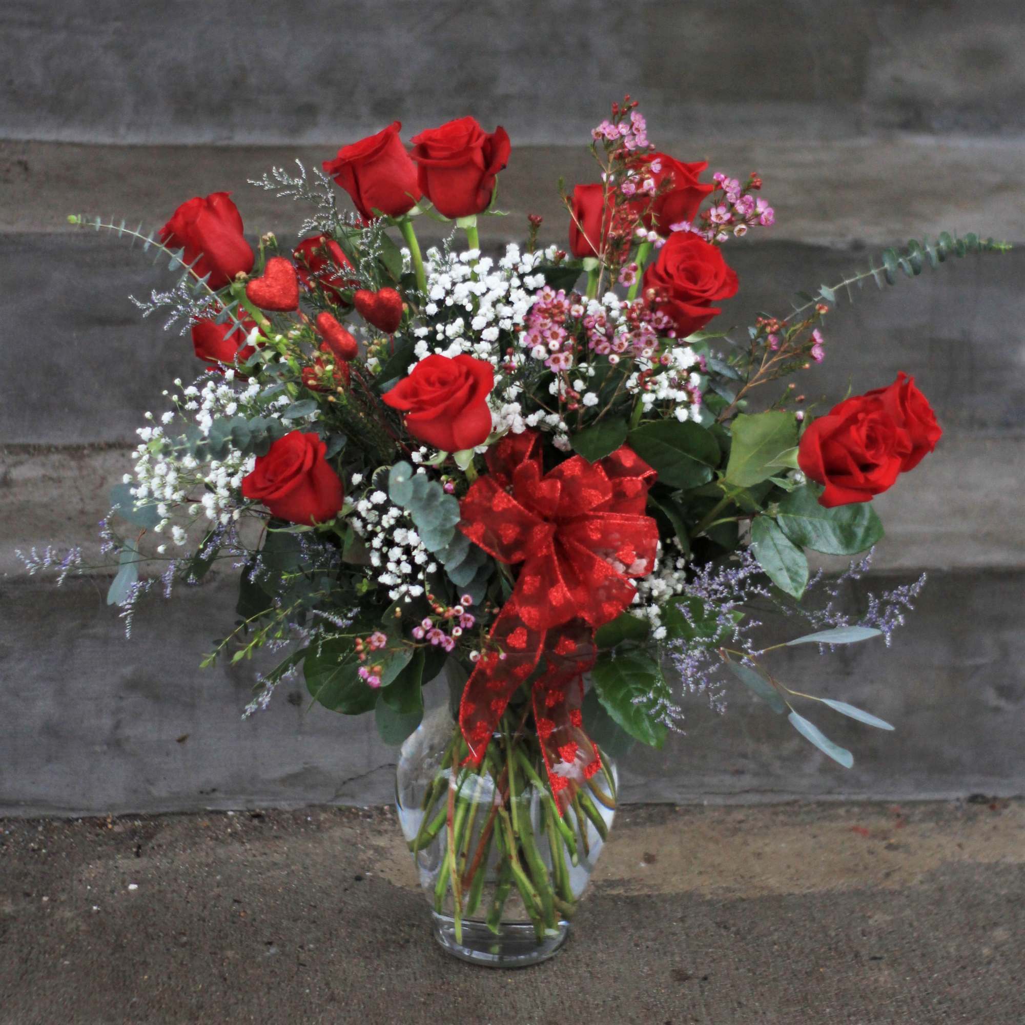 Red roses arranged in a clear glass vase with a red ribbon.
