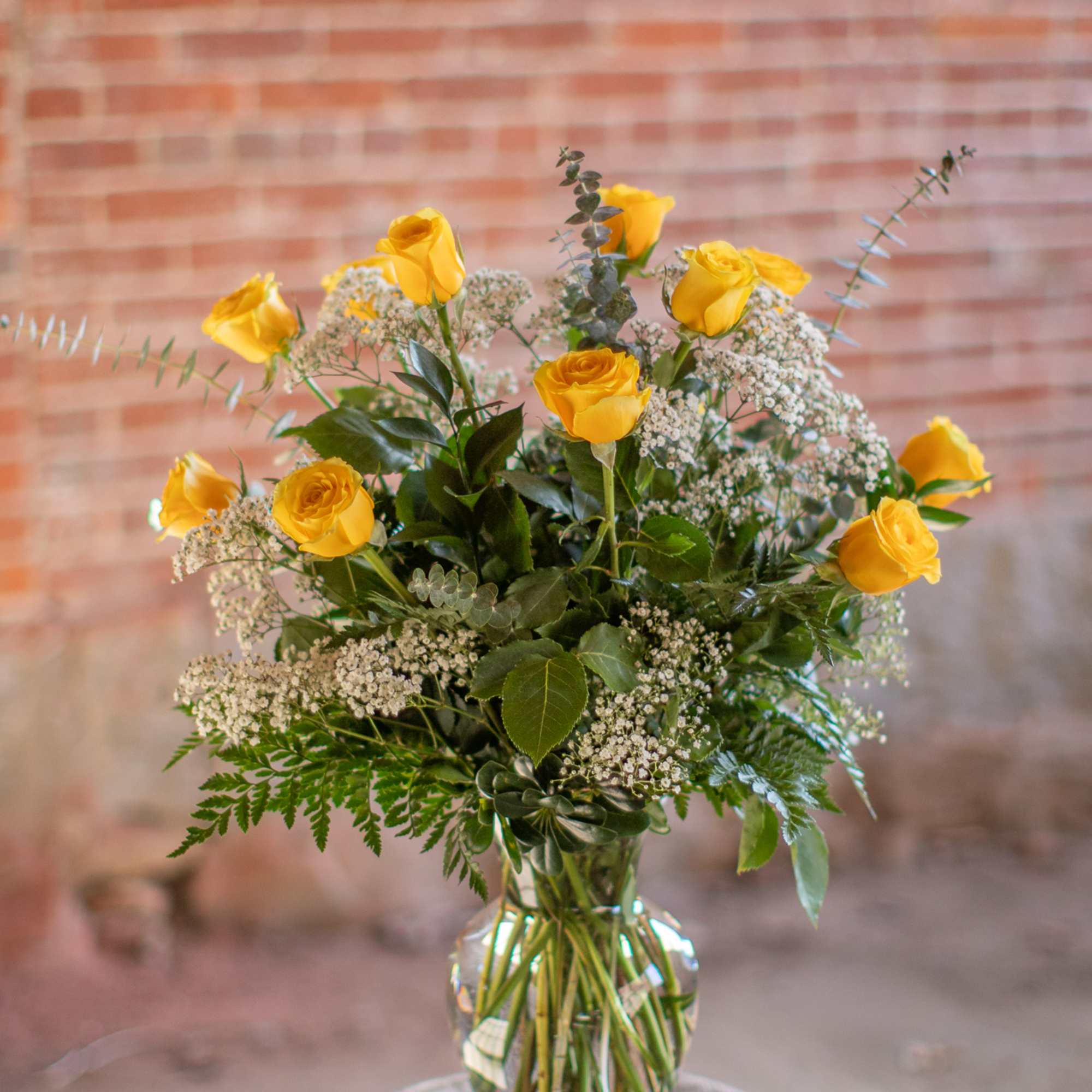 Yellow roses in a clear glass vase with white filler flowers