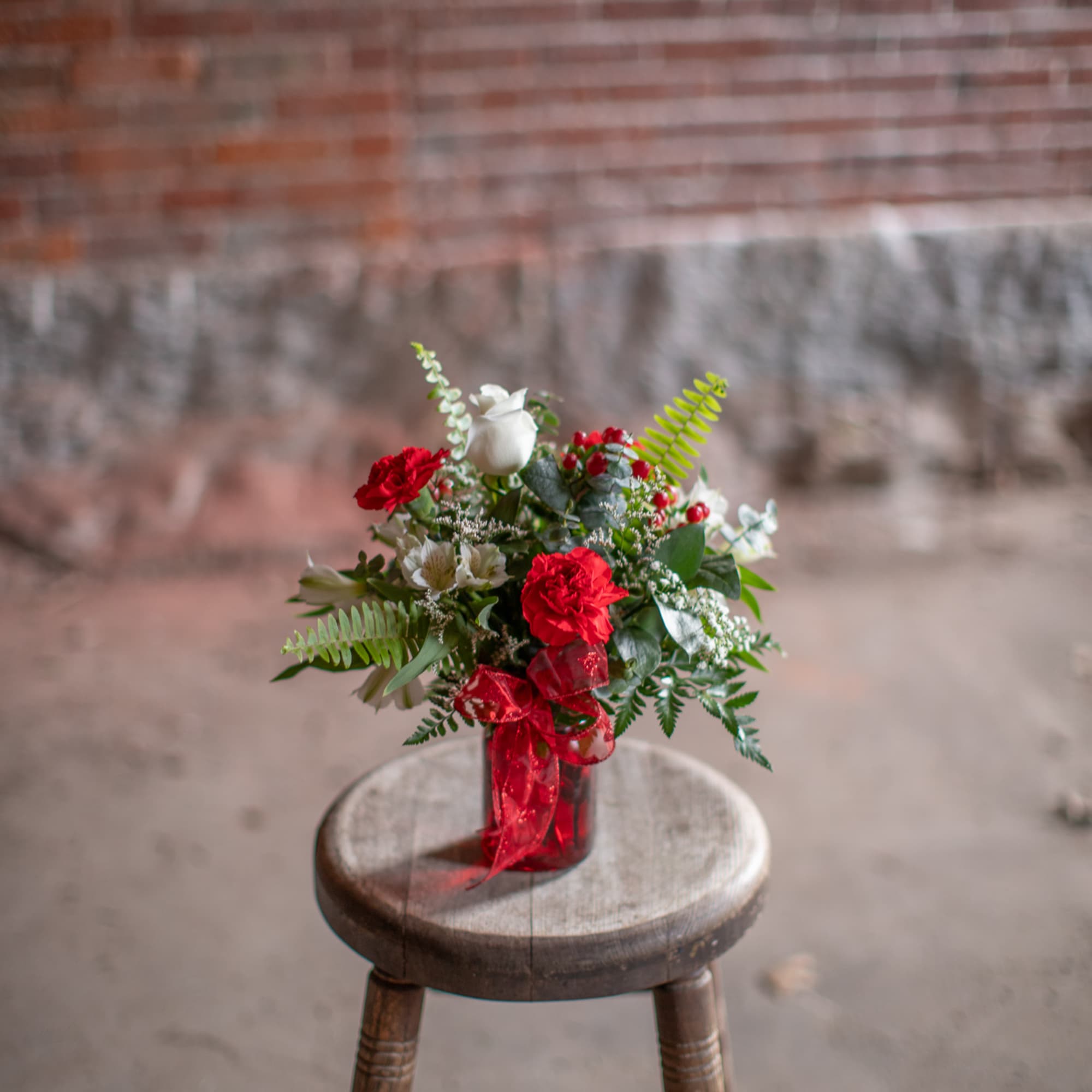 Small bouquet of red and white flowers in a glass vase with a red ribbon