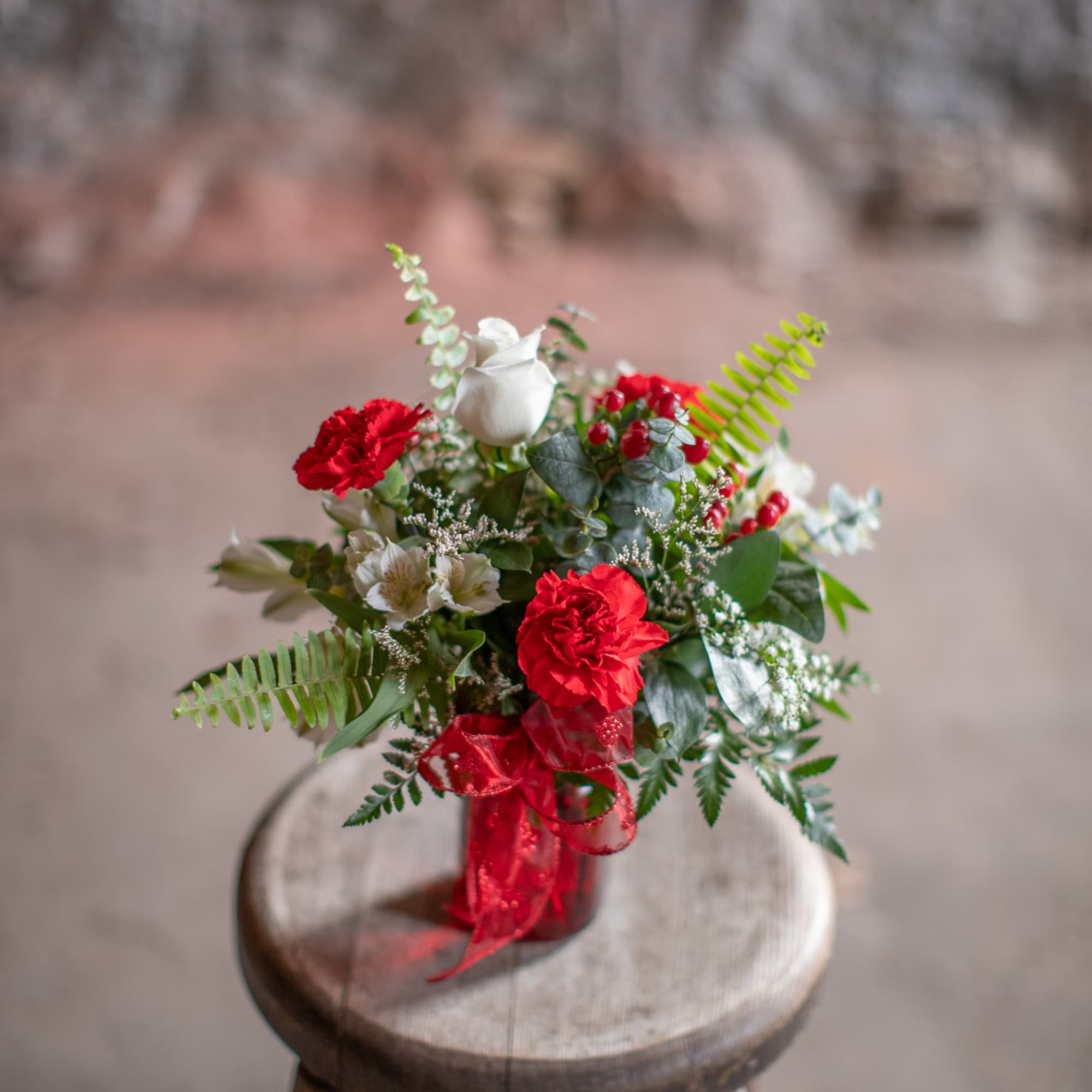 Red and white floral arrangement in a red ribbon-tied vase on a wooden stool