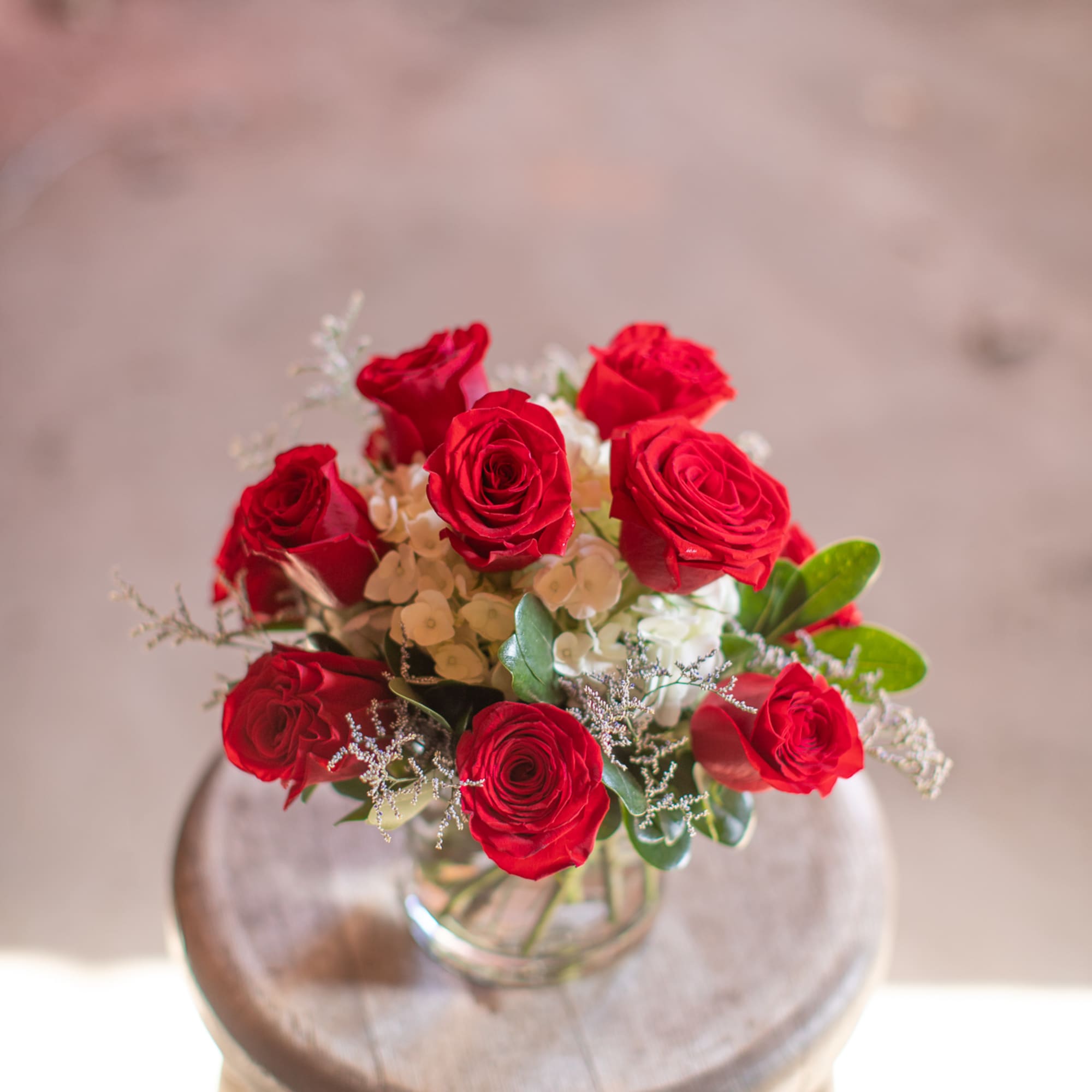 Red roses arranged in a clear glass vase on a stool