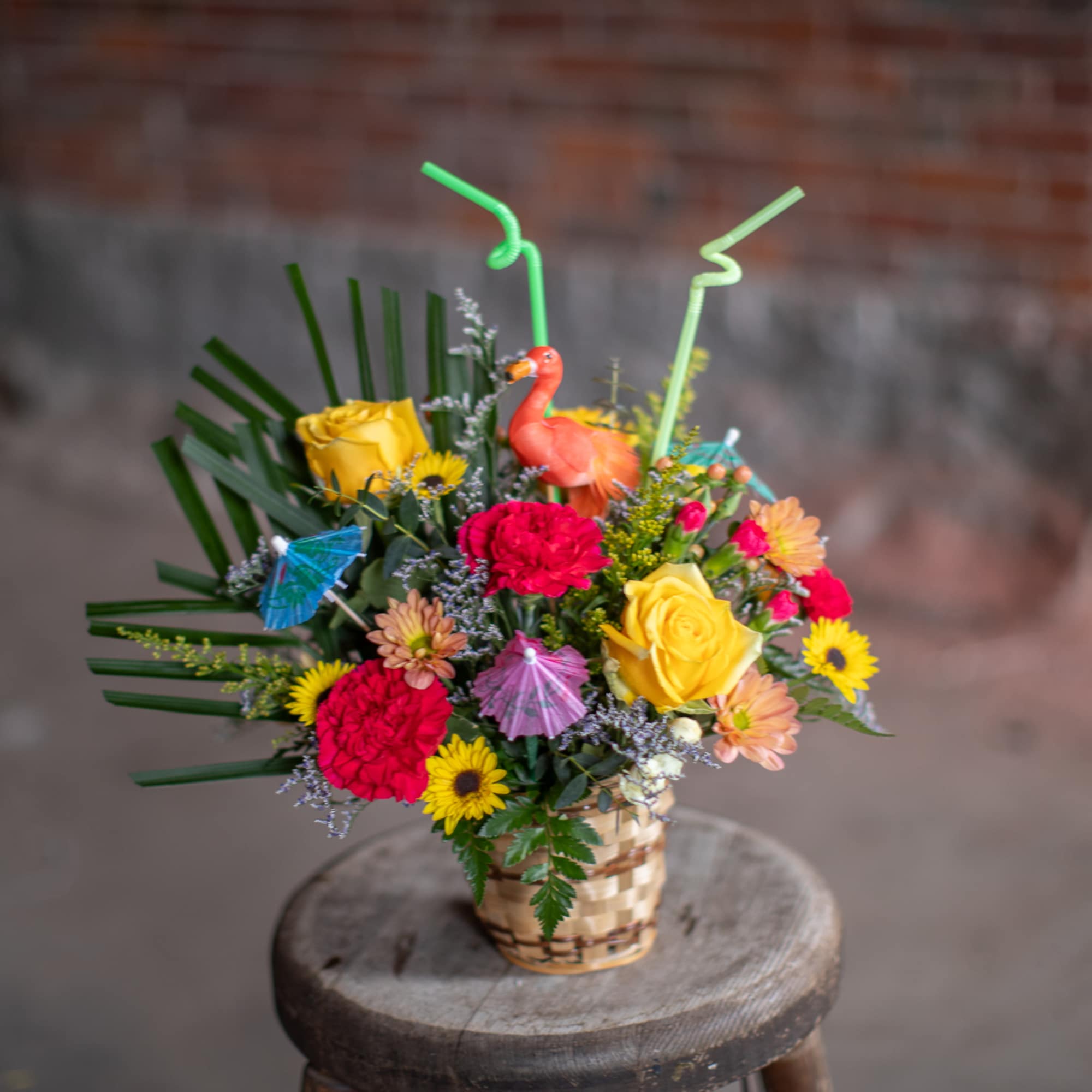 Colorful mixed flower arrangement in a woven basket with small cocktail umbrellas