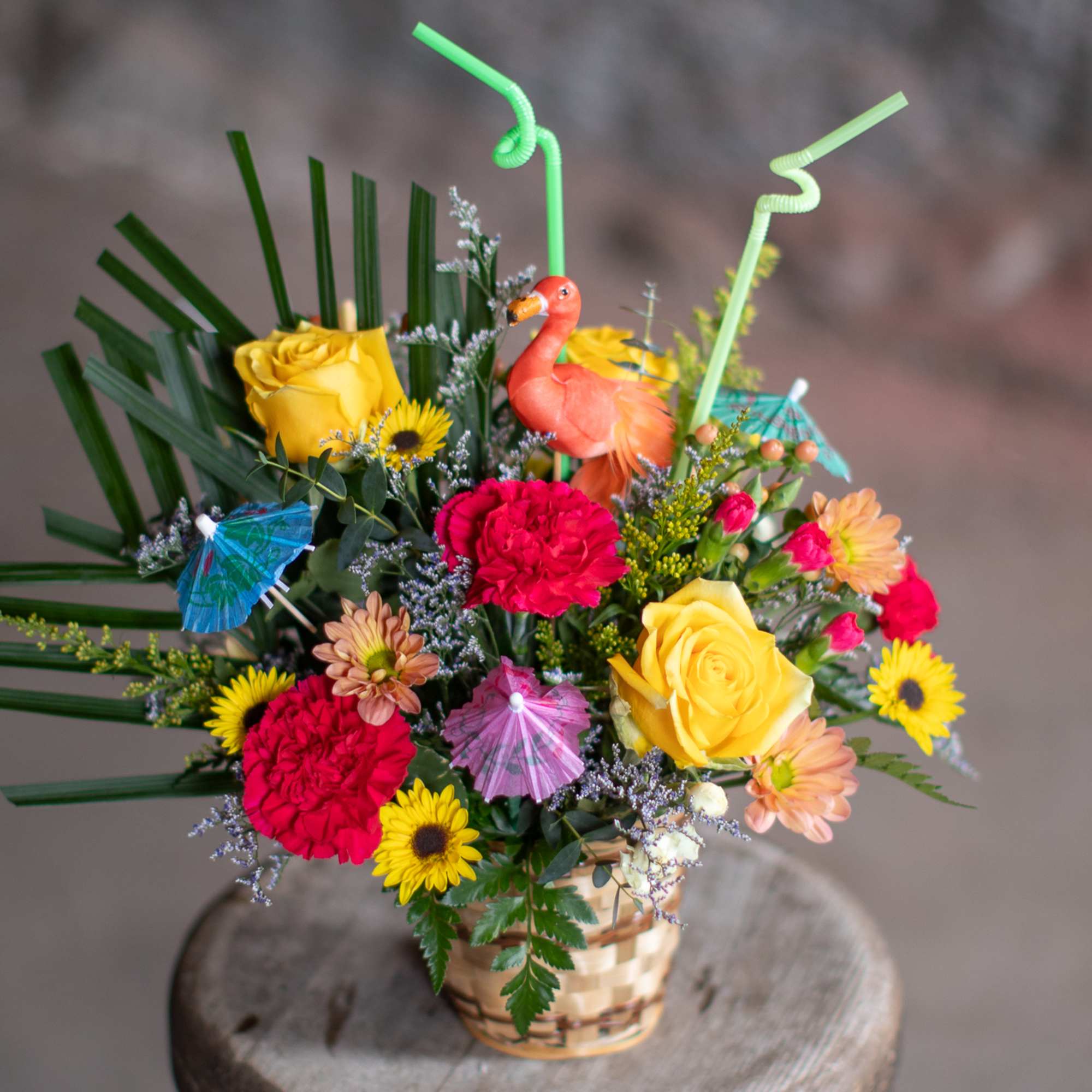 Colorful bouquet in a woven basket with roses, carnations, and small umbrellas