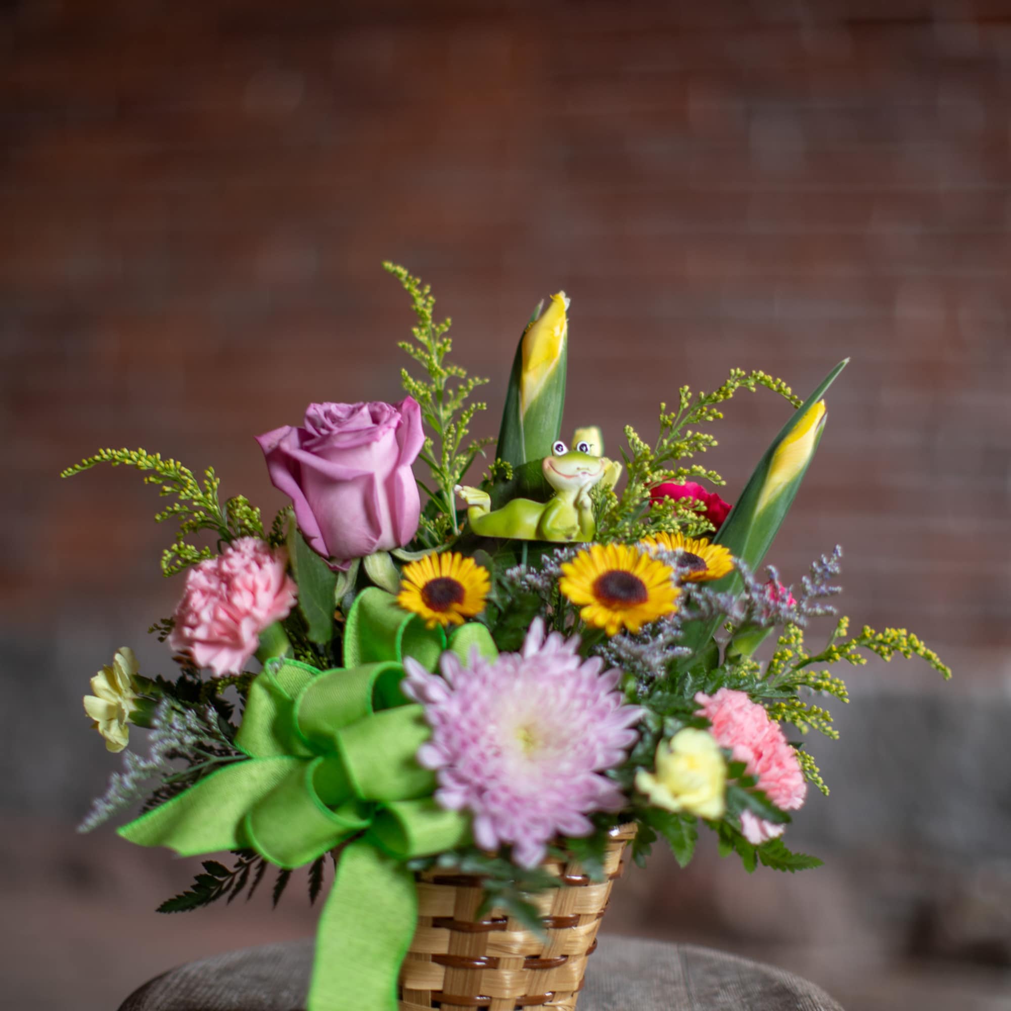 Mixed flower basket with a green ribbon and a small frog figurine