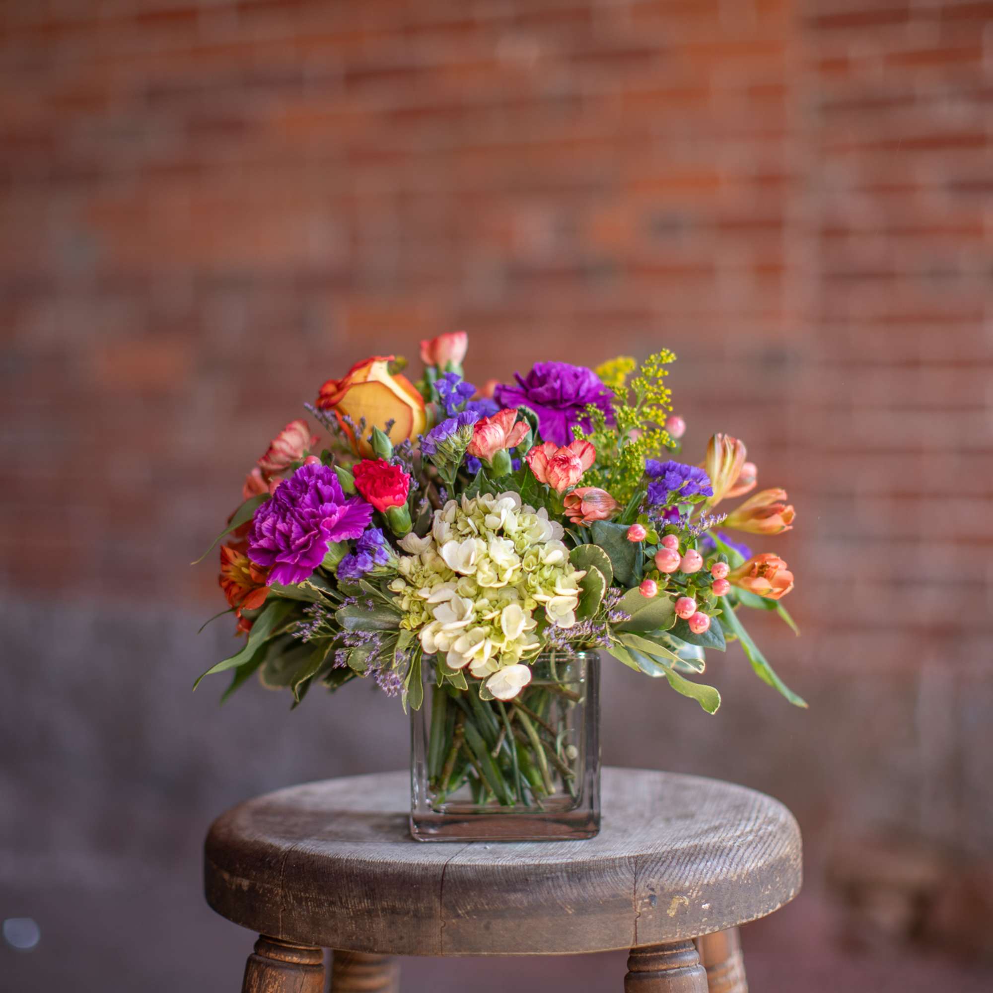 Mixed bouquet in a clear glass vase on a wooden stool