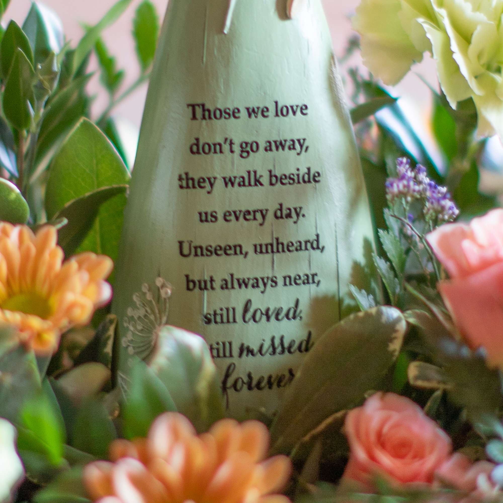 Sympathy figurine with memorial quote surrounded by peach and pink flowers.