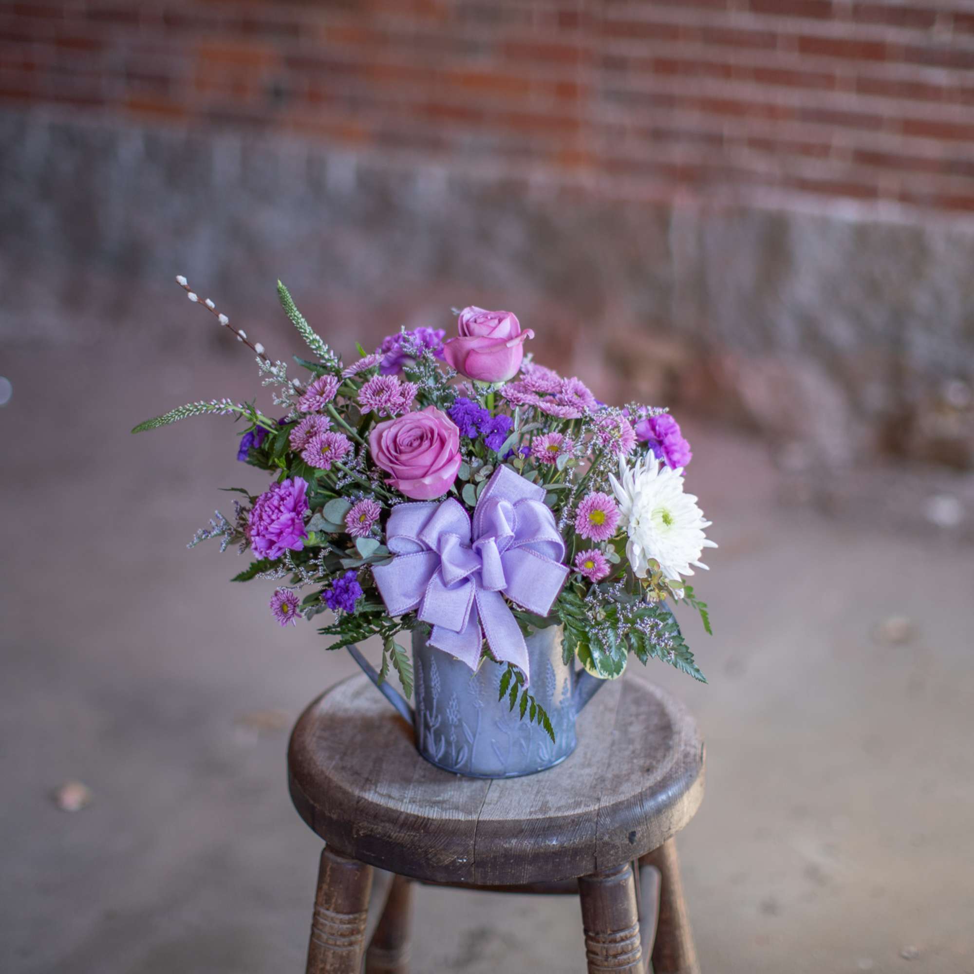 Purple and pink flower arrangement in a blue vase with a lavender bow