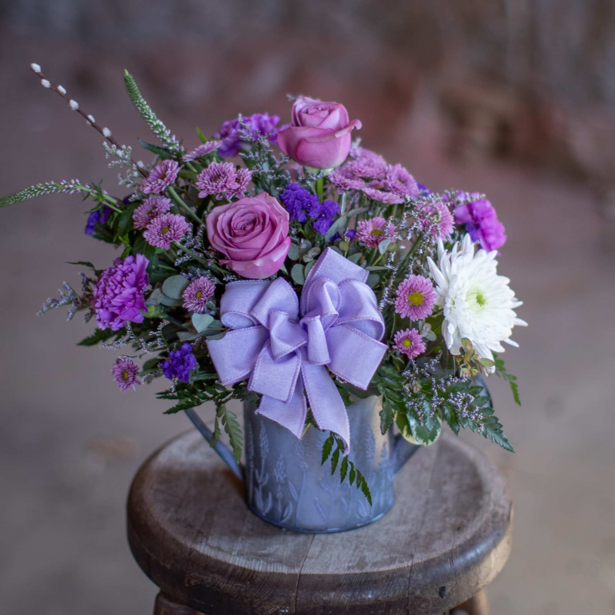 Purple and white flower arrangement in a metal container with a lavender bow