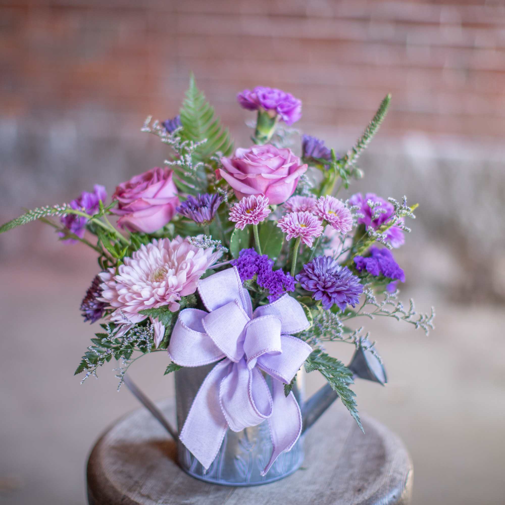 Pink and purple flower arrangement in a metal pail with a lavender ribbon