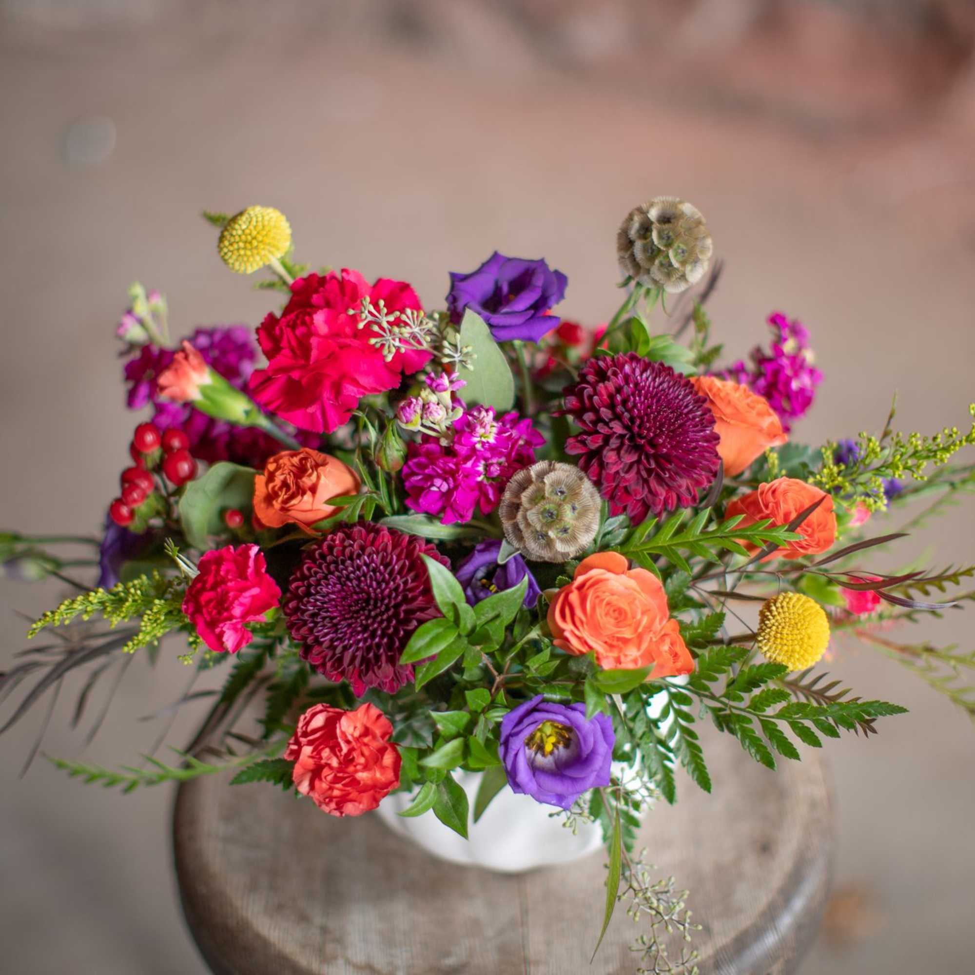 Colorful mixed bouquet in a white vase with orange, pink, purple, and yellow blooms