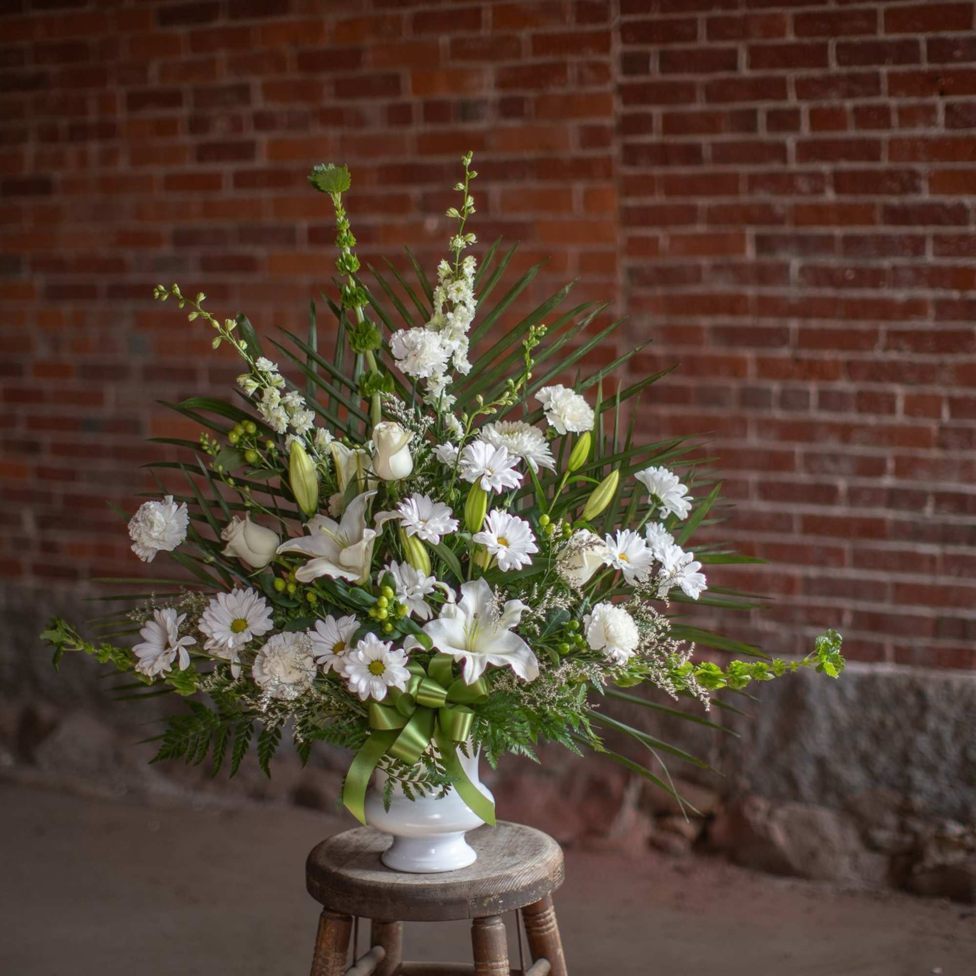 White floral arrangement in a white vase with a green ribbon