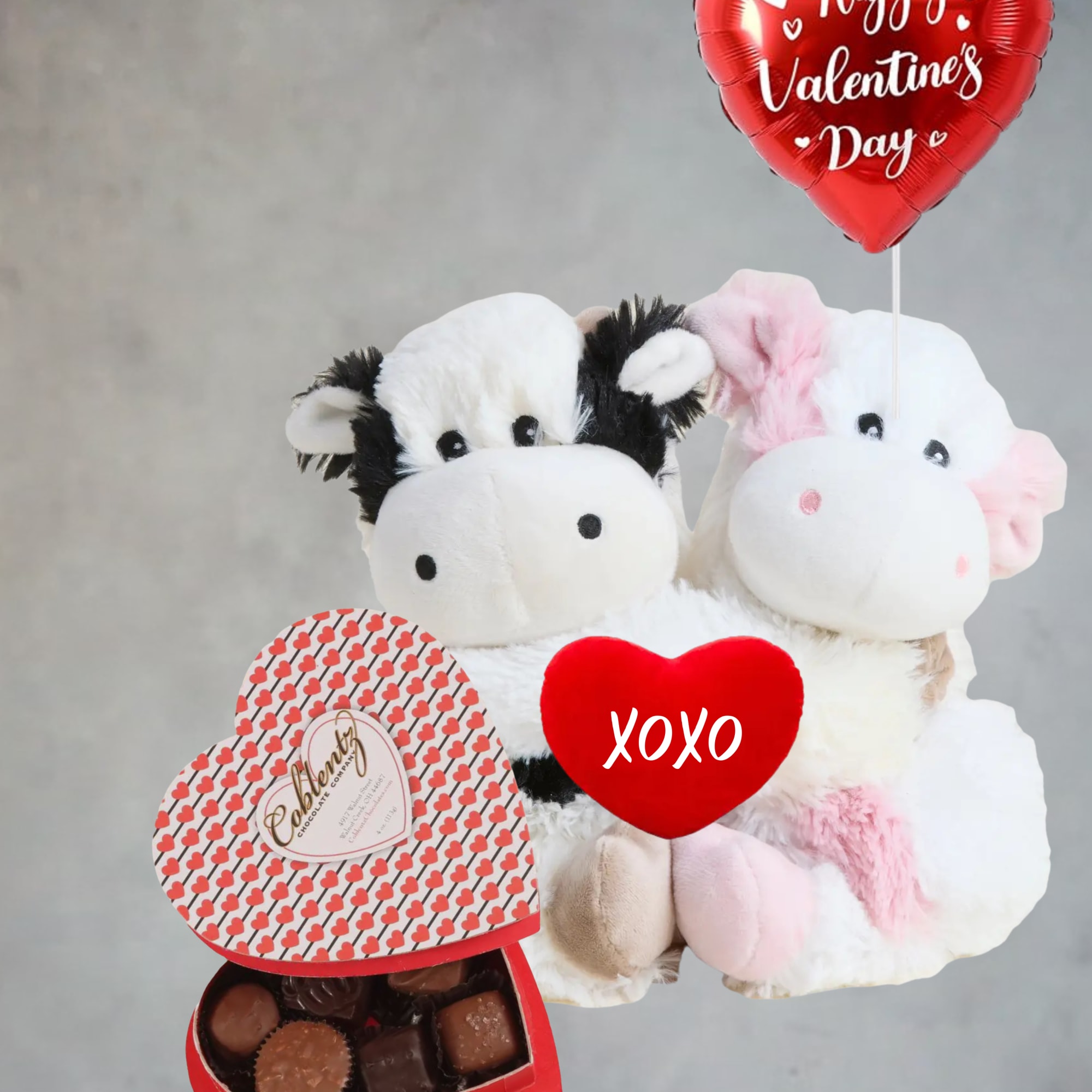 Two plush cows with a heart balloon and chocolate box
