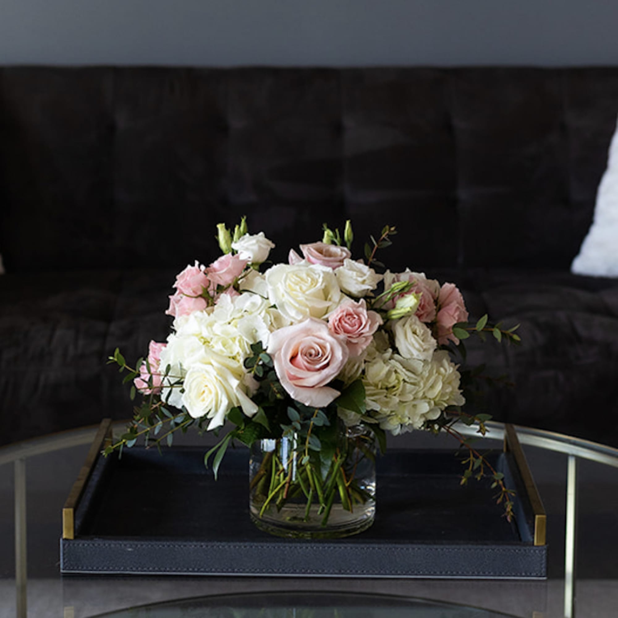 Pink and white roses arranged in a clear glass vase on a coffee table