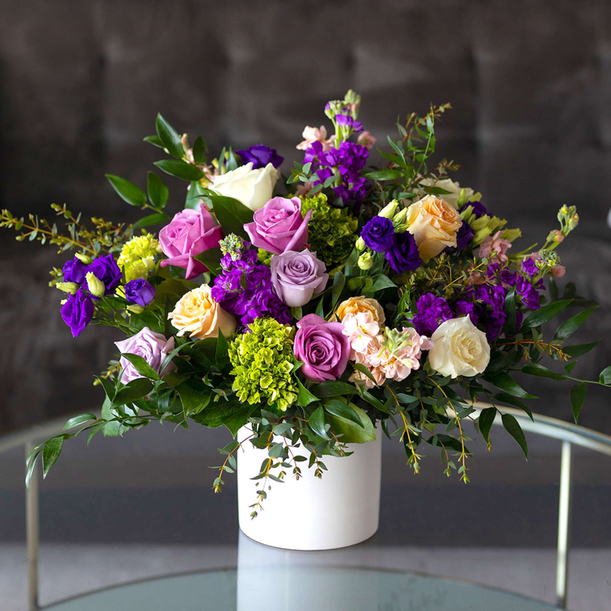 Mixed bouquet of roses and purple blooms in a white vase