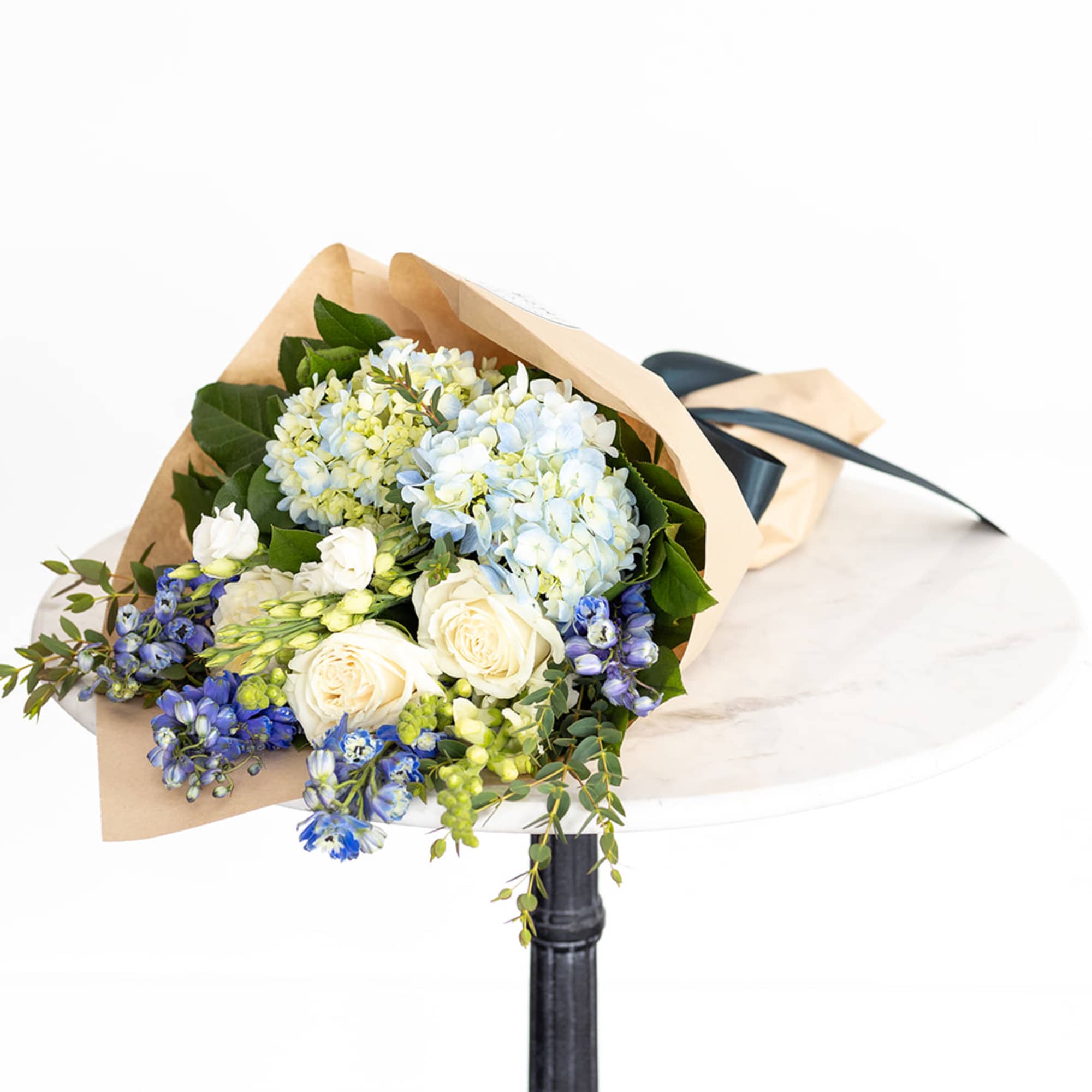 Bouquet of blue hydrangeas, white roses, and blue flowers wrapped in paper