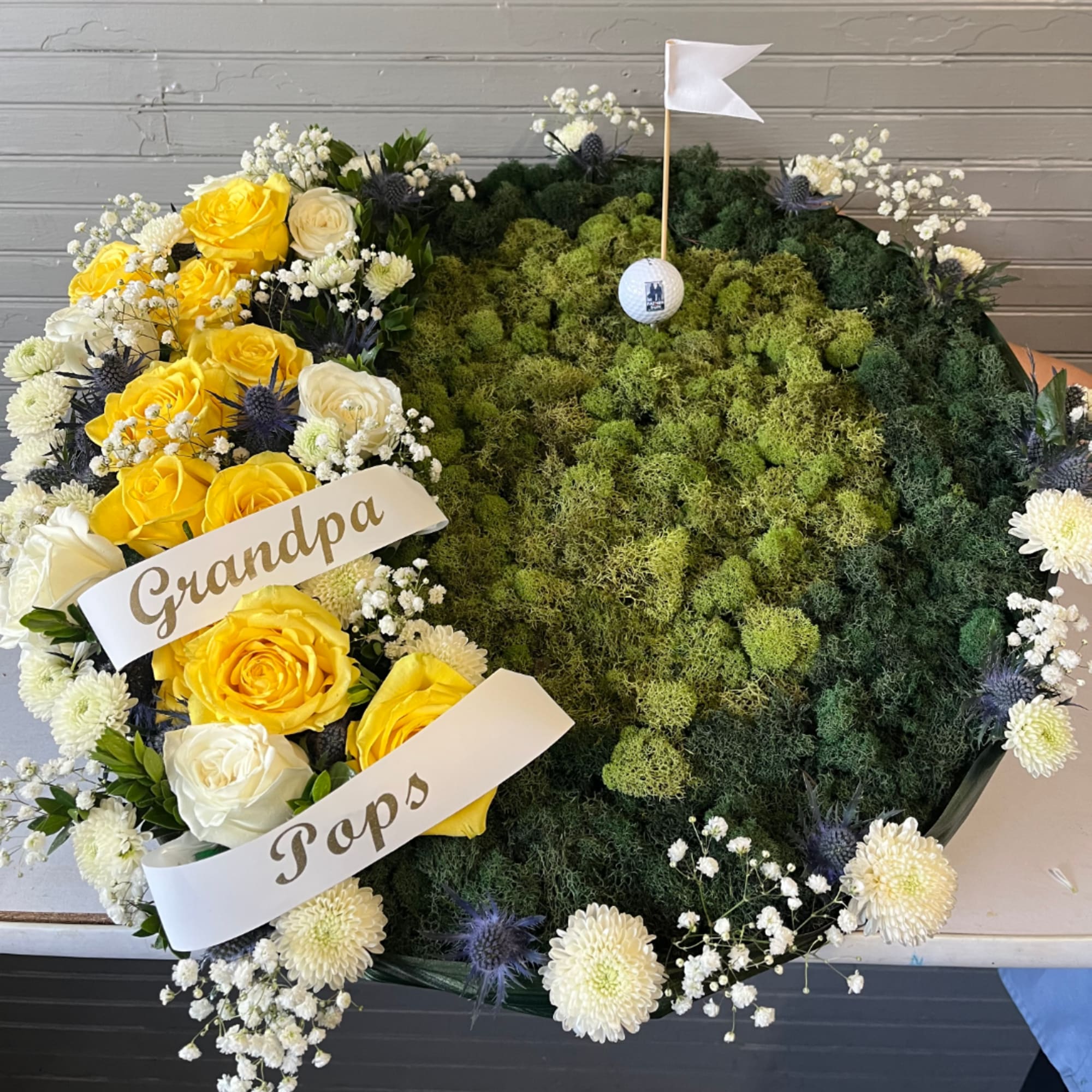 Heart-shaped floral tribute with yellow and white roses and moss center