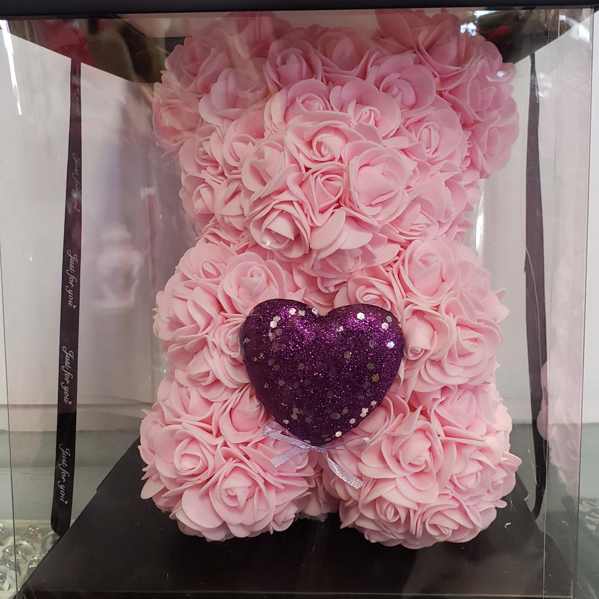 Pink rose-shaped teddy bear with a purple glitter heart in a clear box