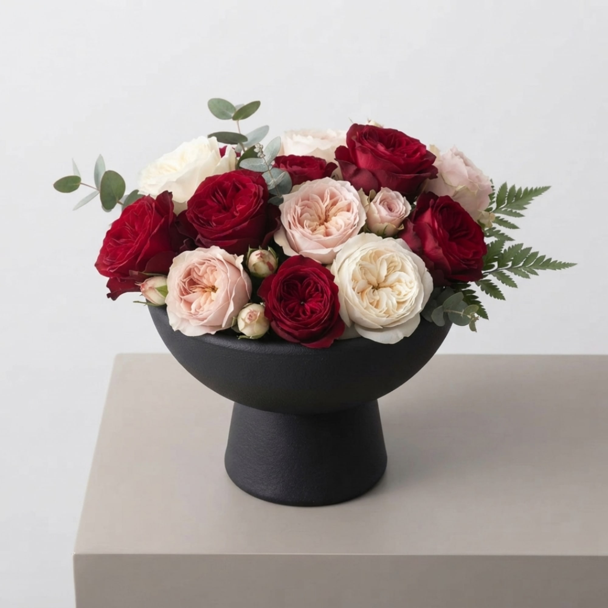 Red and blush roses arranged in a black pedestal vase