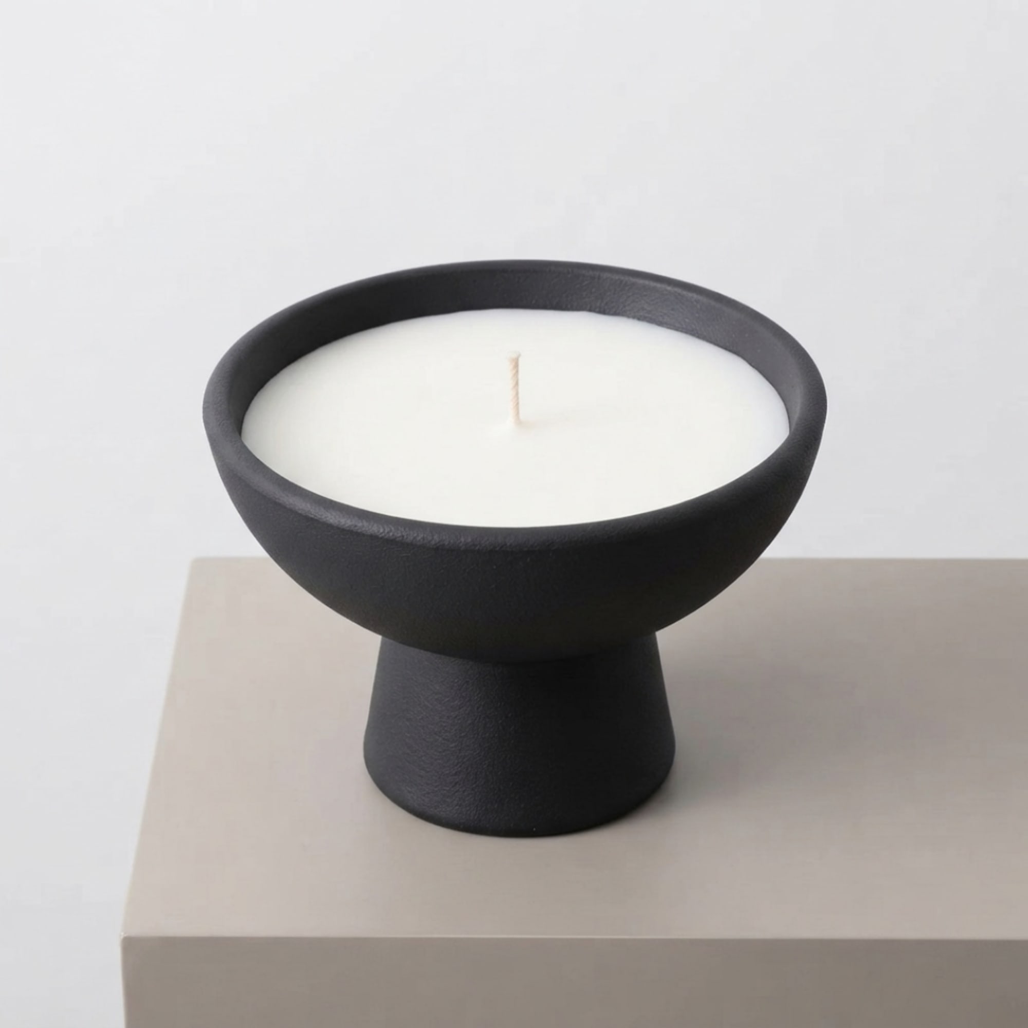 White candle in a black pedestal bowl on a beige surface