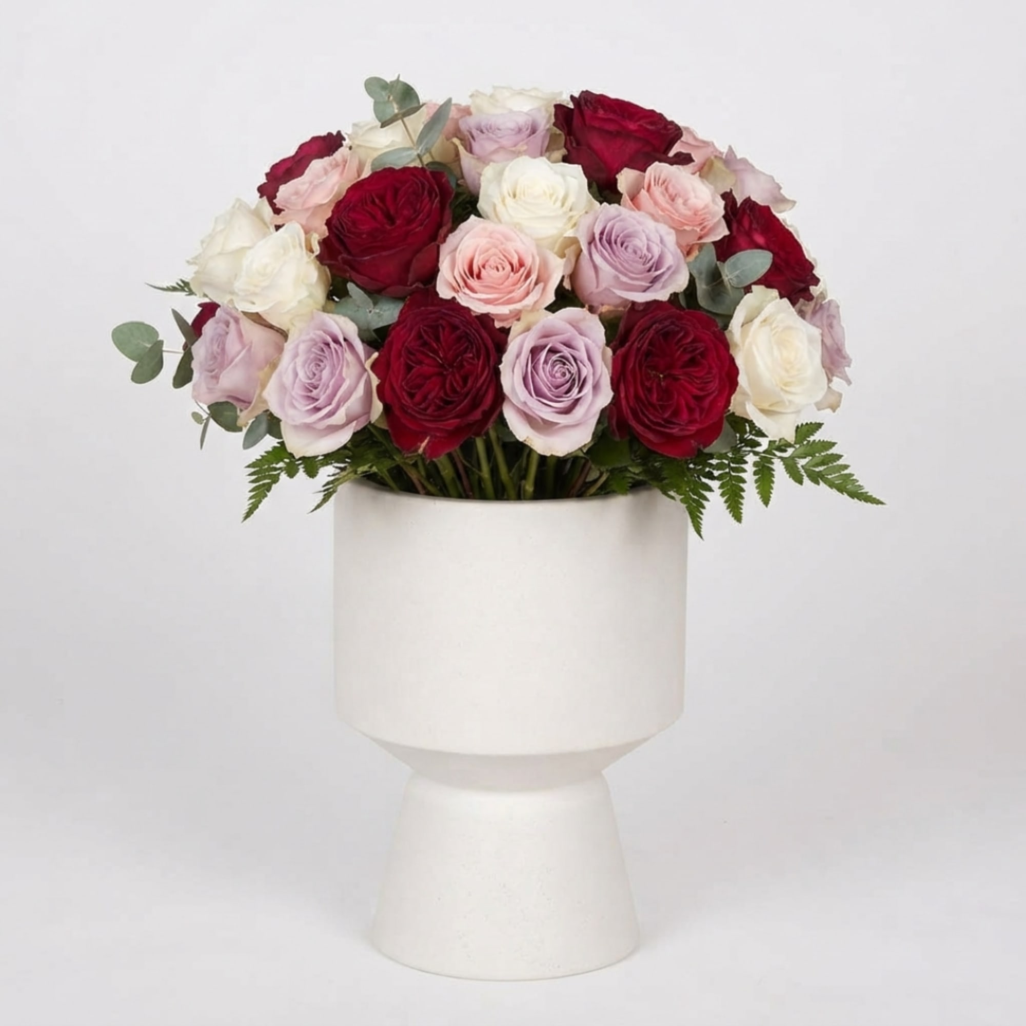 Bouquet of red, pink, white, and lavender roses in a white pedestal vase