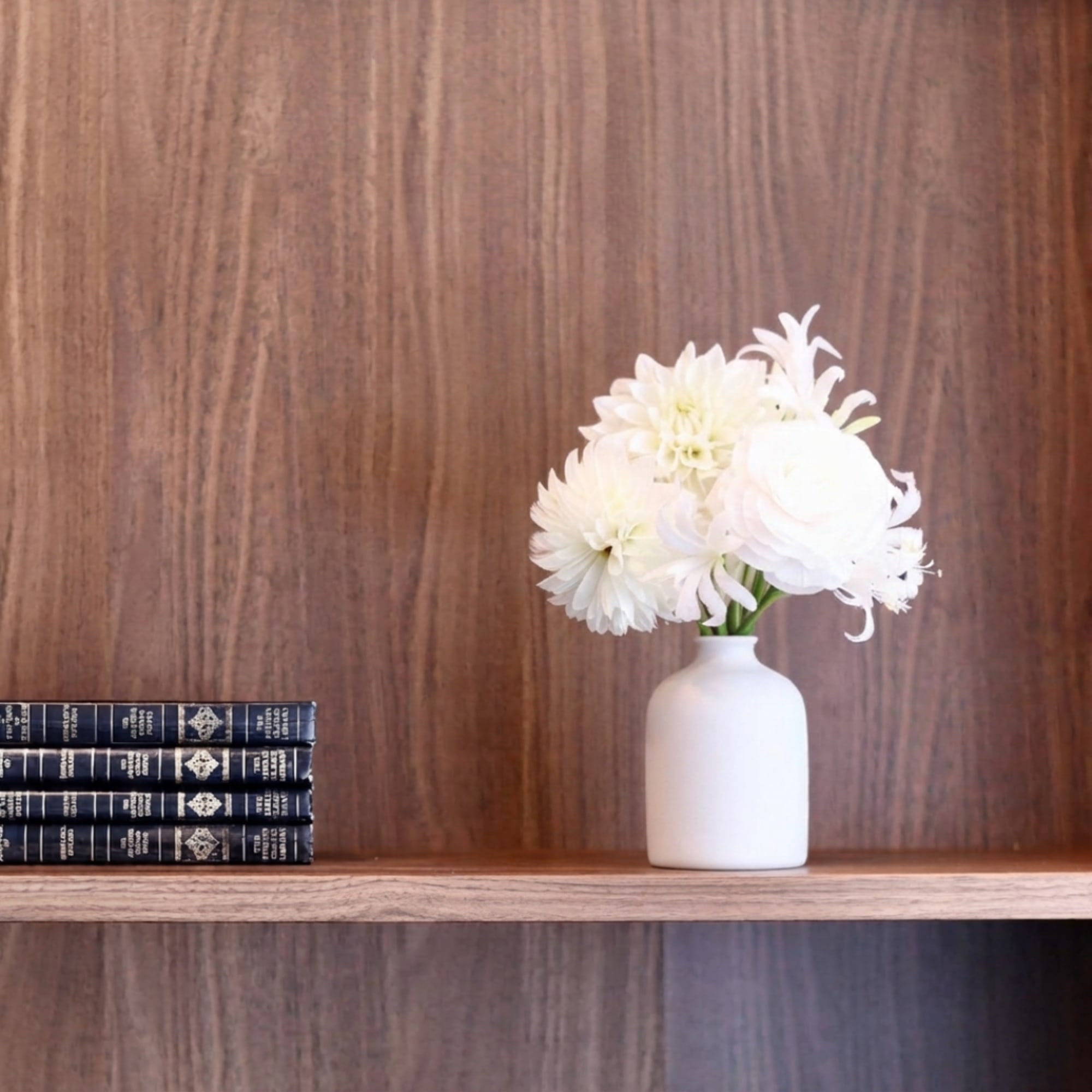 White flowers arranged in a small white vase on a wooden shelf