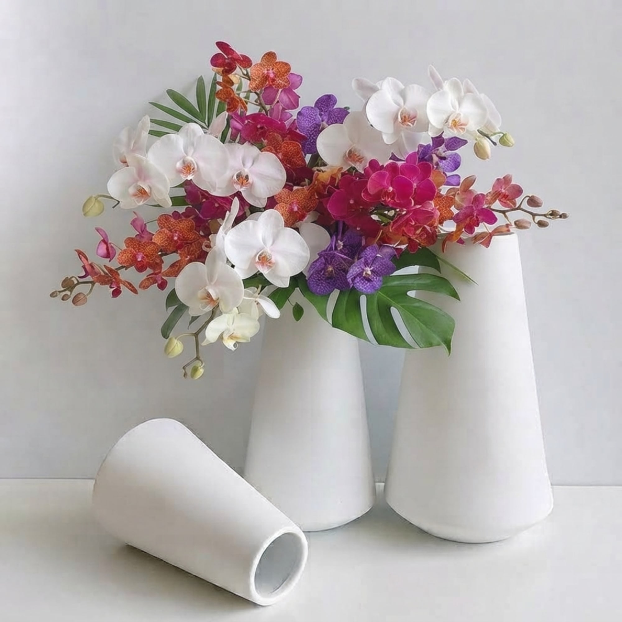 Arrangement of white, pink, purple, and orange orchids in white cone vases