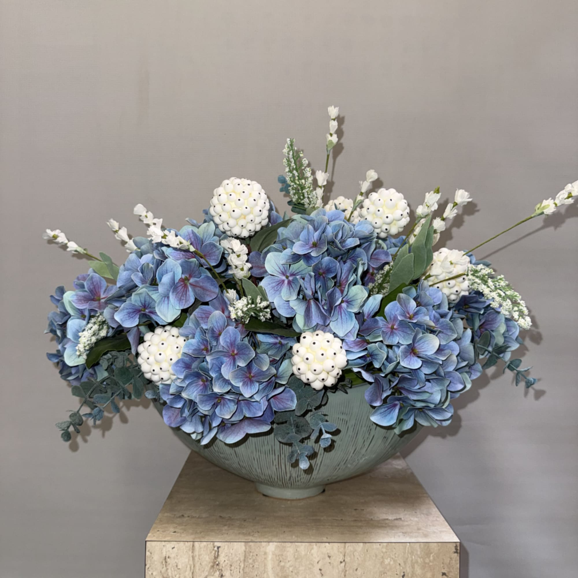 Blue hydrangea arrangement in a pale ceramic bowl with white accent flowers