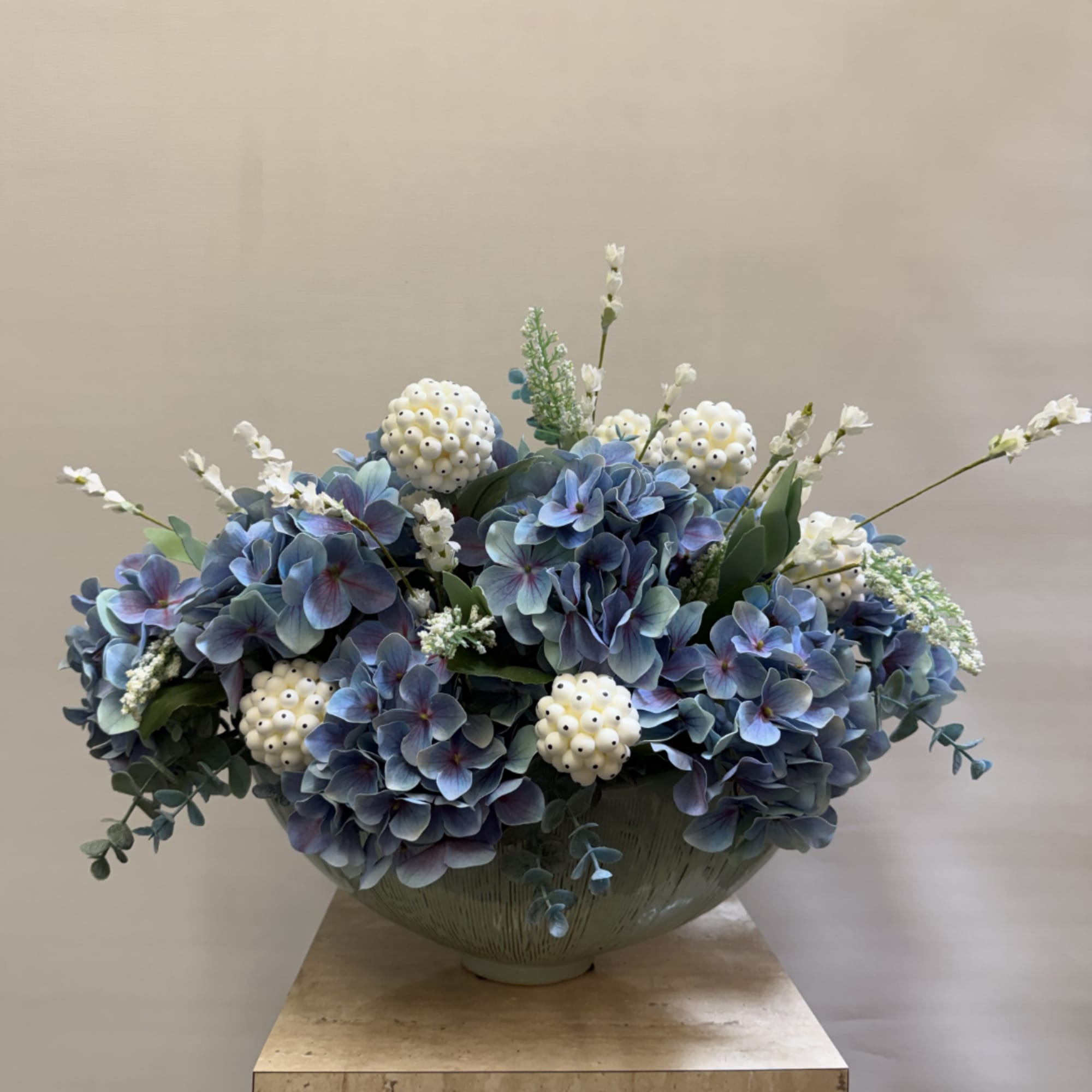 Blue hydrangea arrangement in a low ceramic bowl with white berry accents