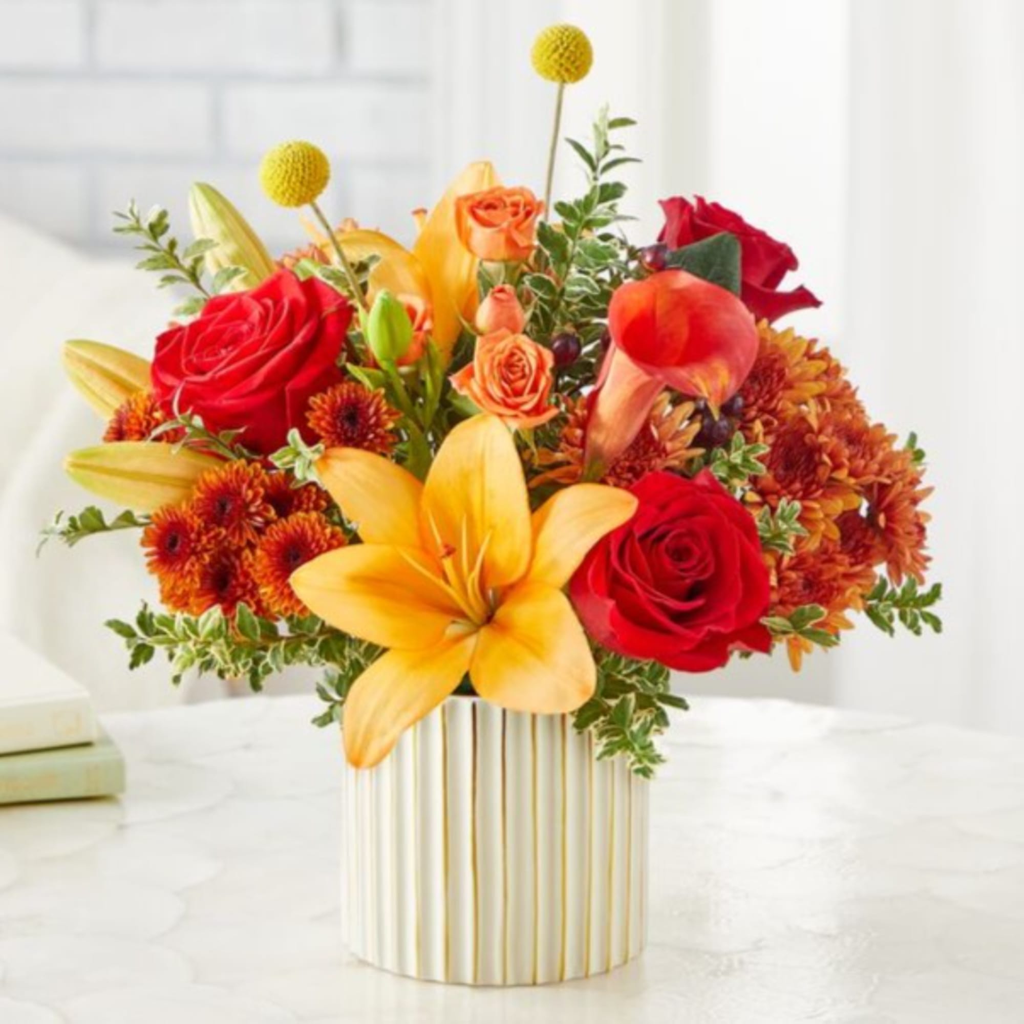 Bouquet of red roses, yellow lilies, and orange flowers in a striped vase