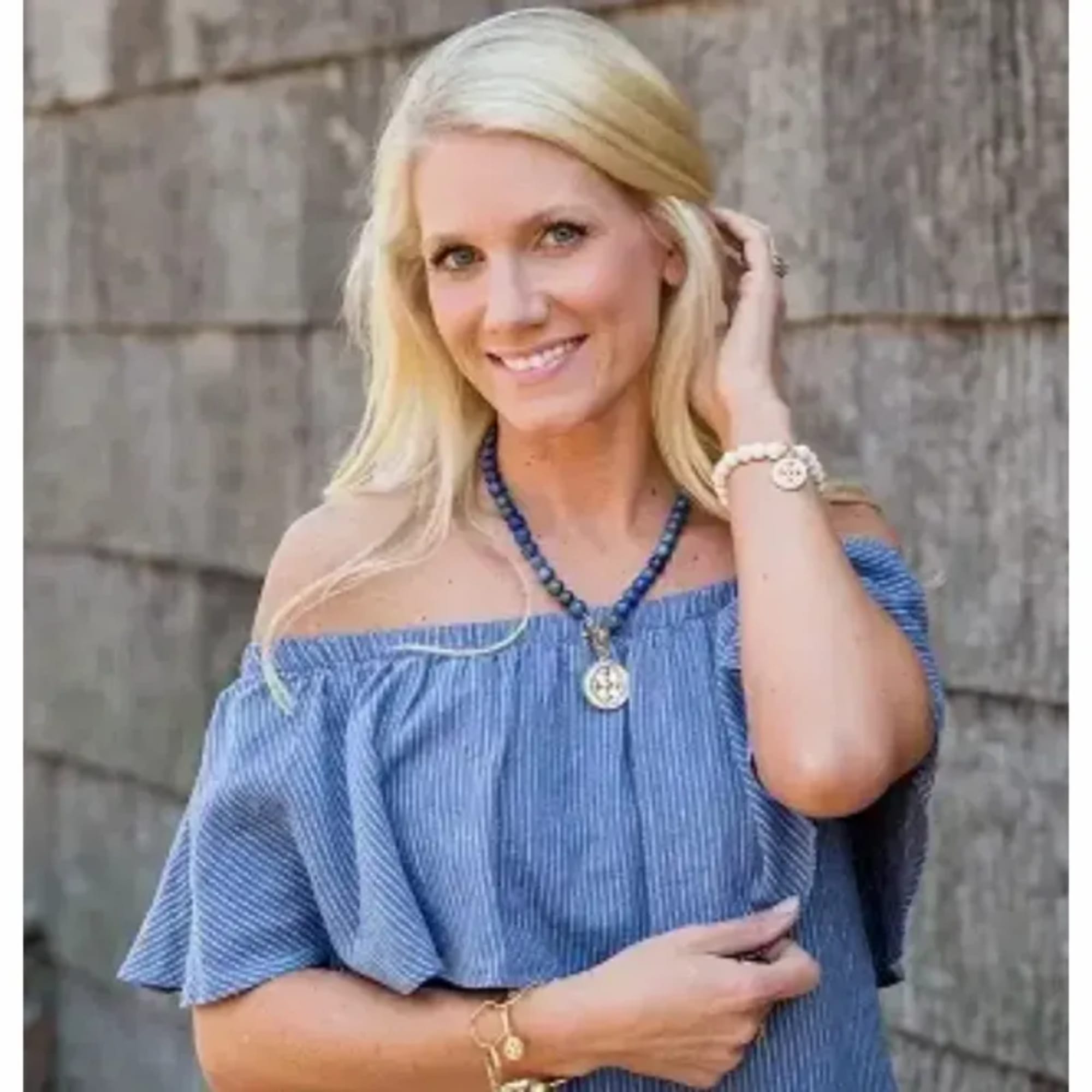 Smiling blonde woman in a blue off-shoulder top with jewelry